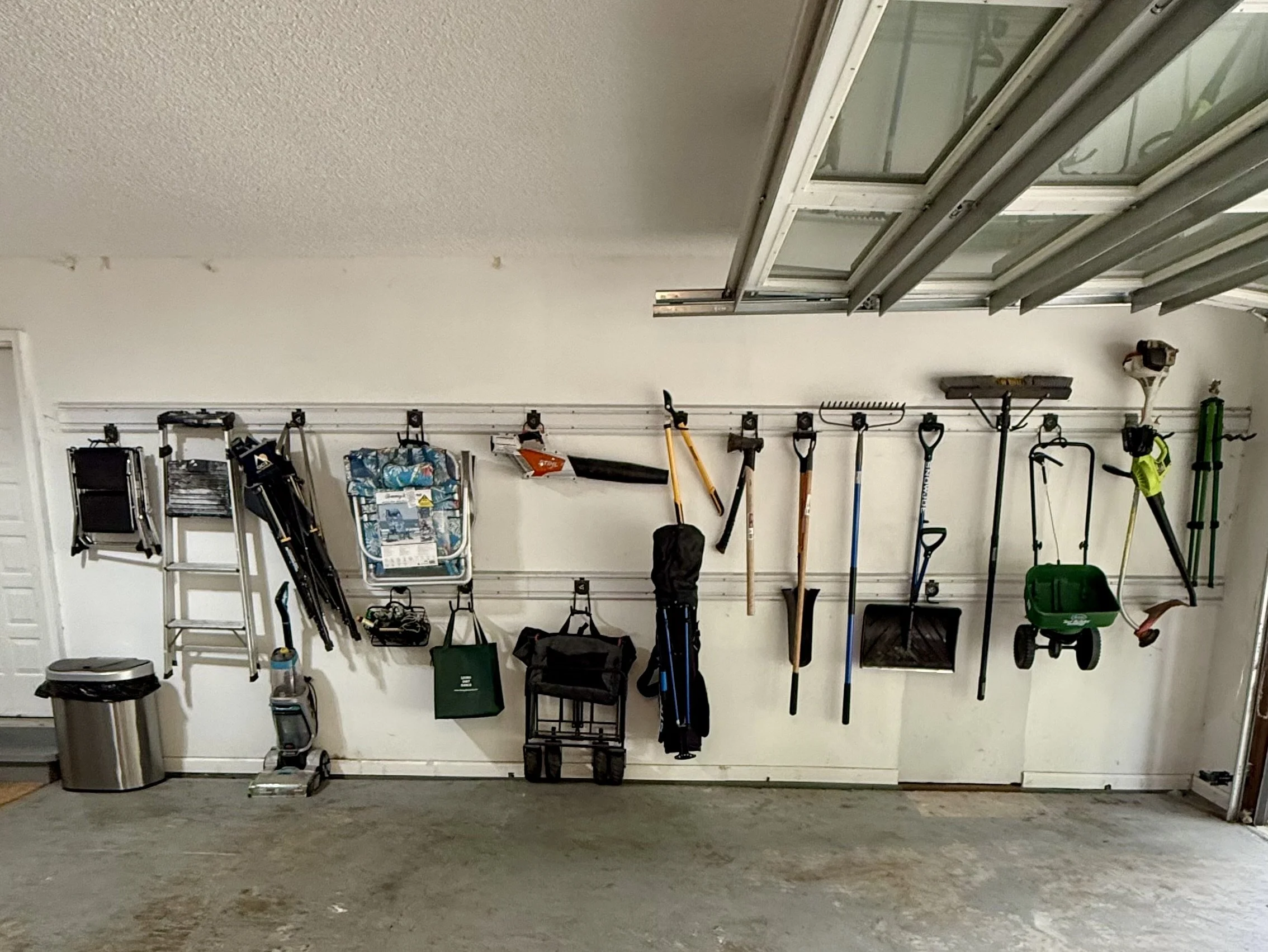 A garage in Parkville with various gardening tools and equipment hanging, including shovels, a rake, a leaf blower, and a wheelbarrow.