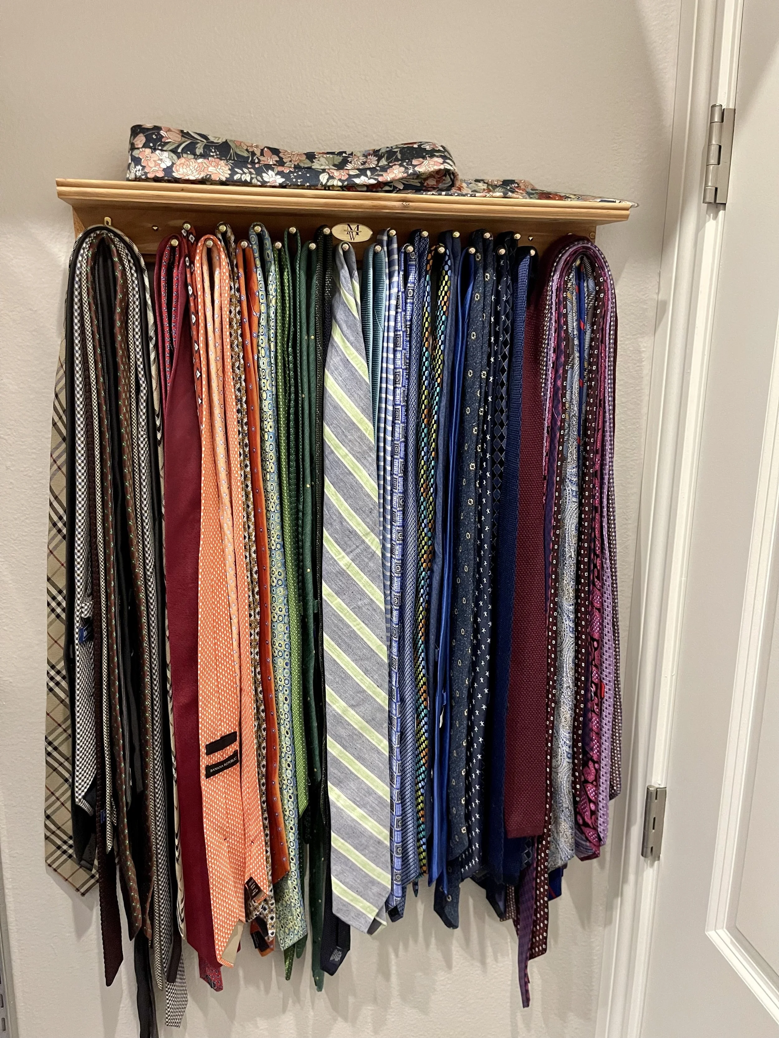 An organized collection of men's neckties hanging on hooks on a wooden rack, with a floral fabric item placed on top.
