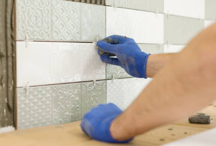 Close-up of Ray wearing blue gloves tiling a wall with patterned tiles in Muskoka
