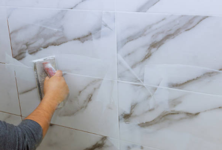 Hand applying grout to gray marble bathroom wall tiles with a float tool