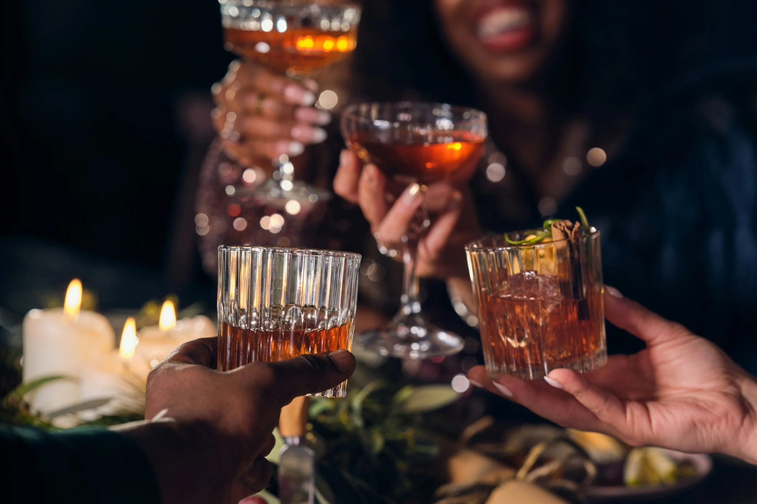 People clinking glasses of drinks at a celebration, with candles and desserts in the background.