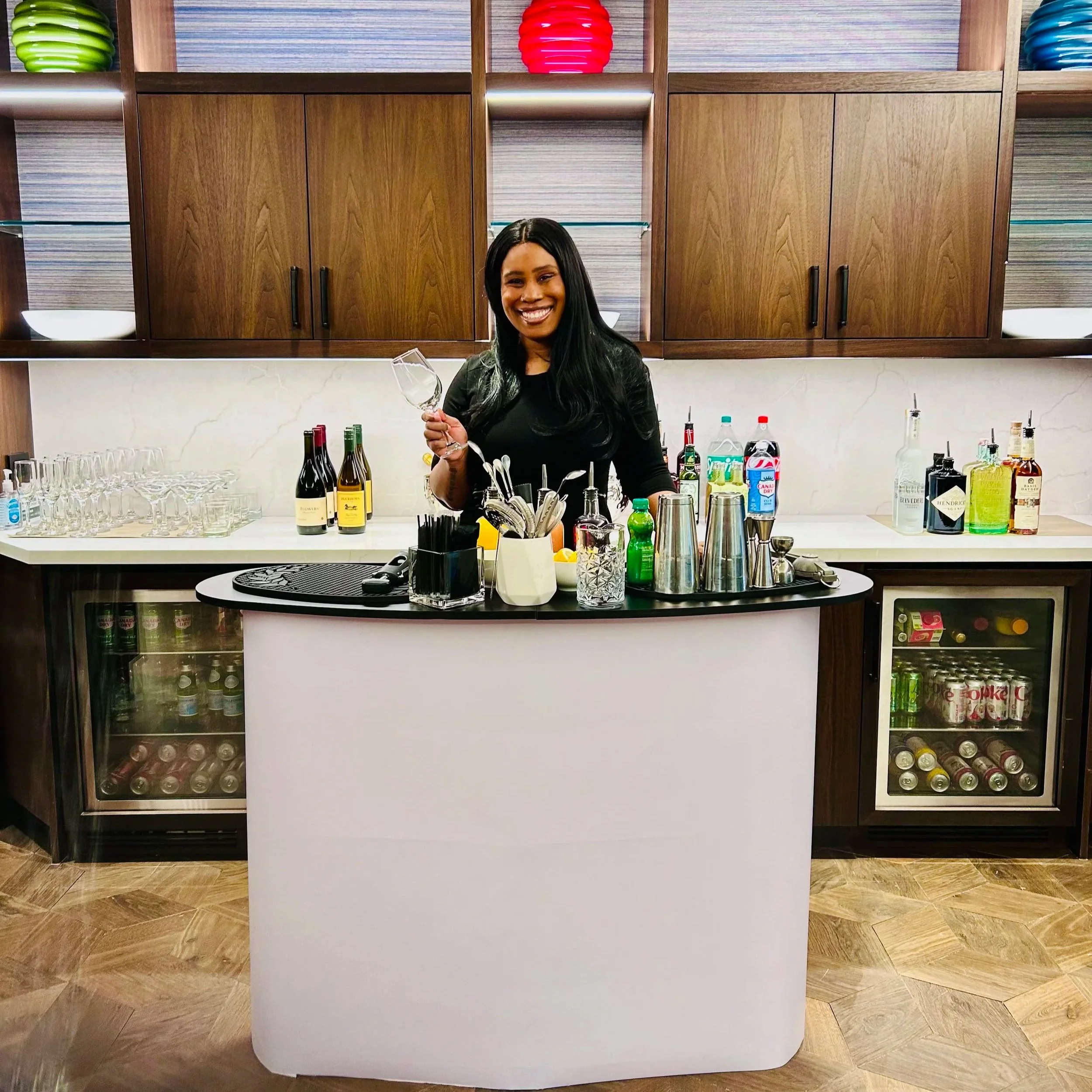 Smiling Brooklyn based bartender in a striped shirt standing behind a bar with liquor bottles, shakers, and citrus fruits.