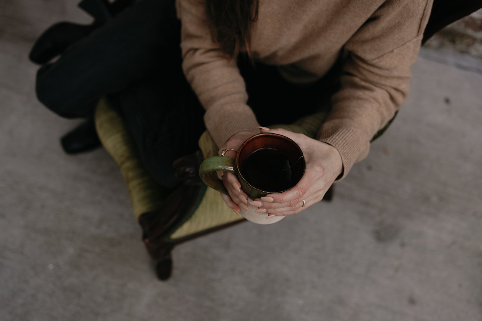 Person sitting on a chair holding a mug of black coffee, seen from above.