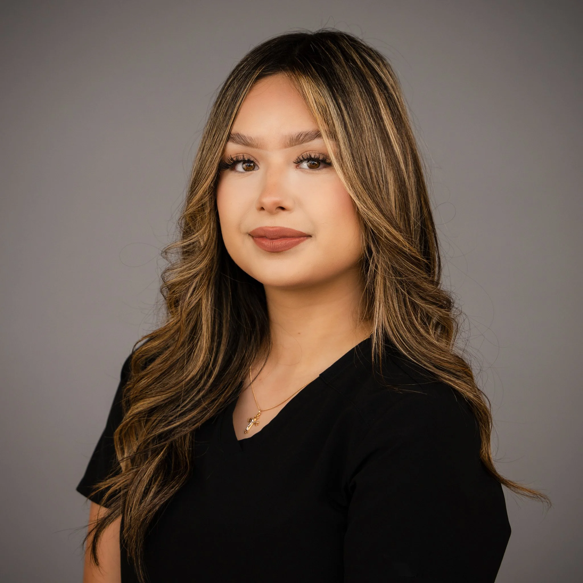 Woman smiling with long dark hair, wearing a black top, and a blurred outdoor background.