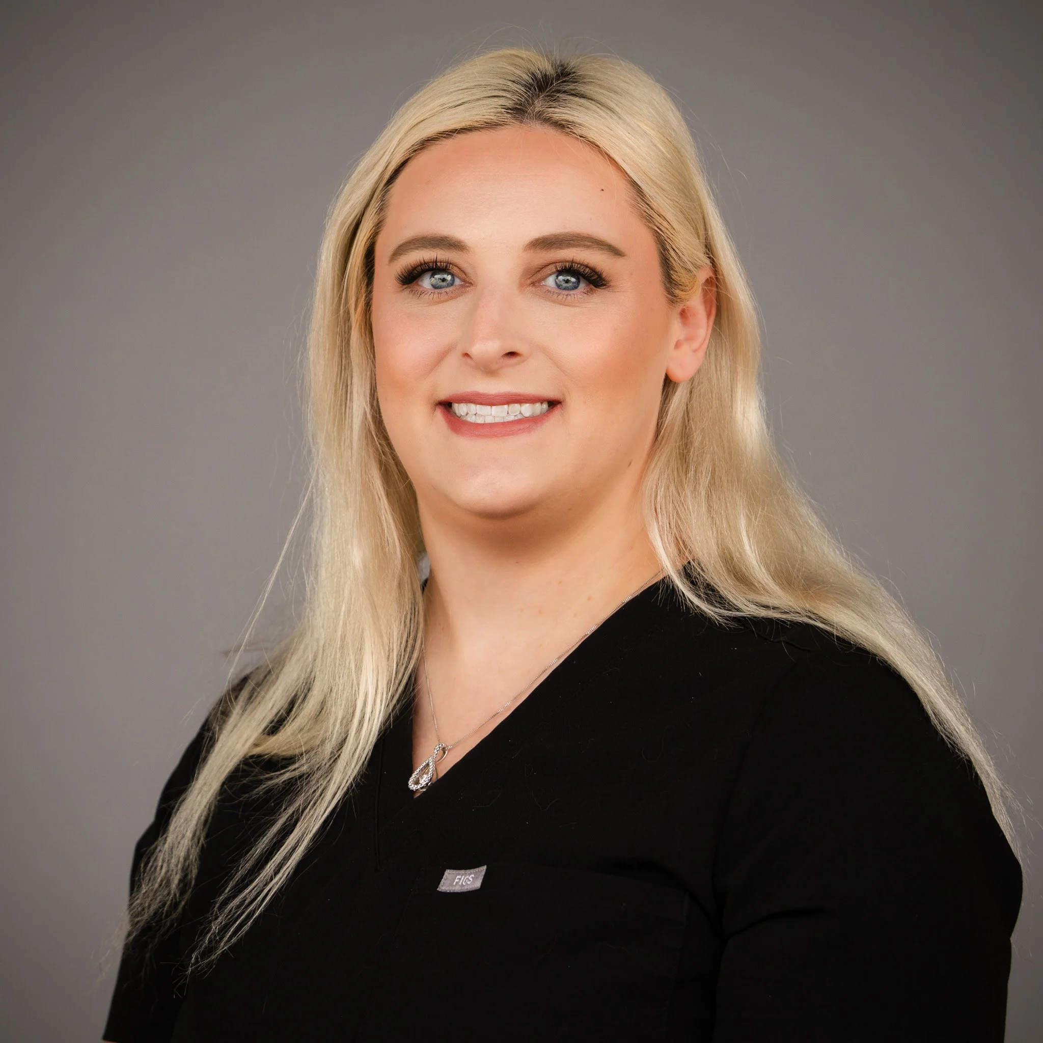 Person smiling with glasses and wearing a black top, standing in front of a brick wall.