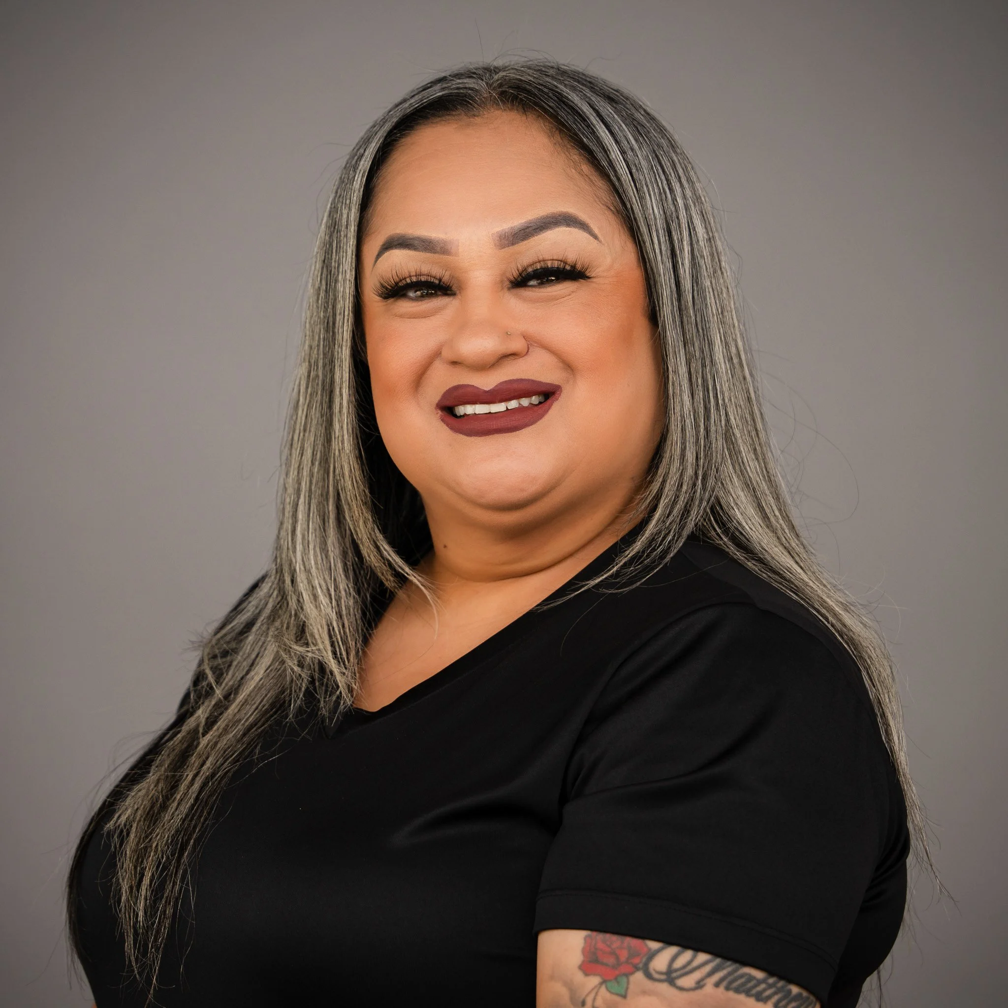 Smiling woman with long hair and makeup, wearing a black top.