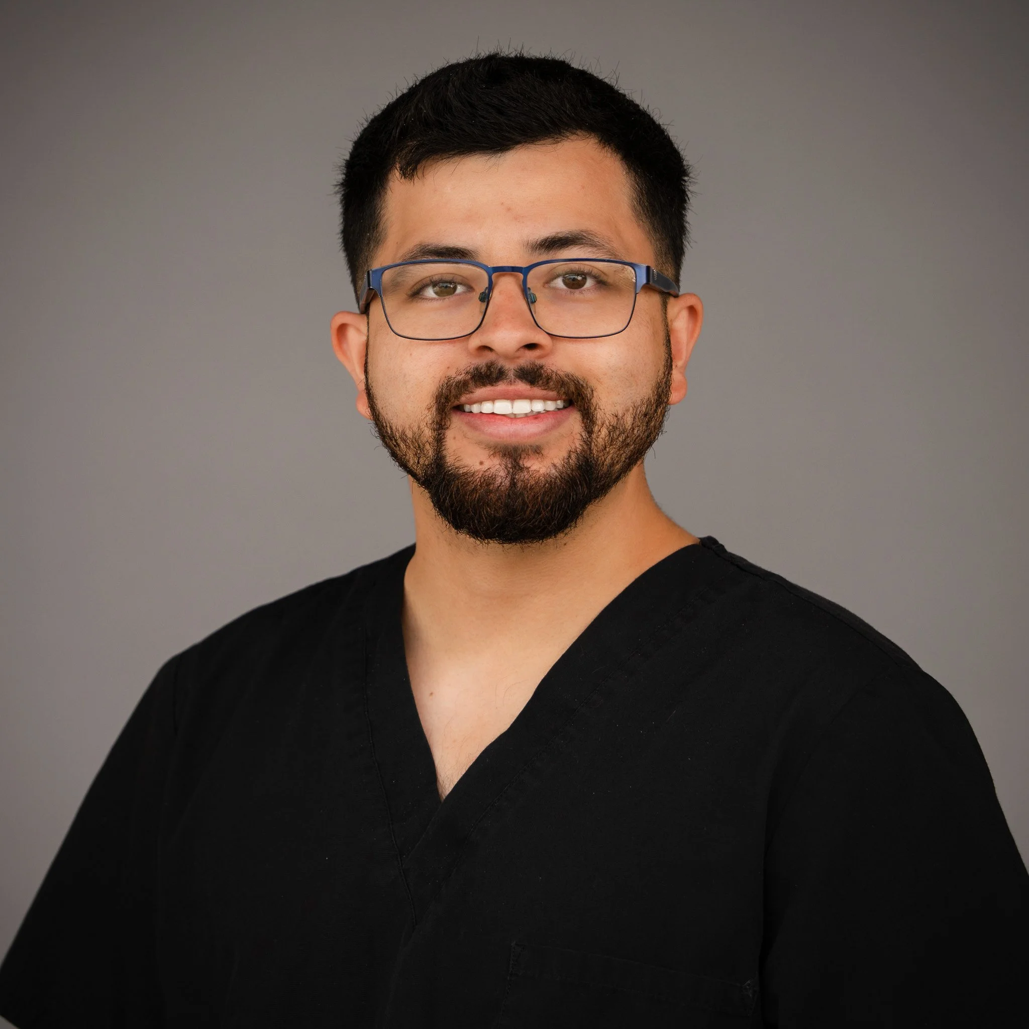 Smiling woman with long, wavy hair wearing a black top, standing in front of a blurred background.