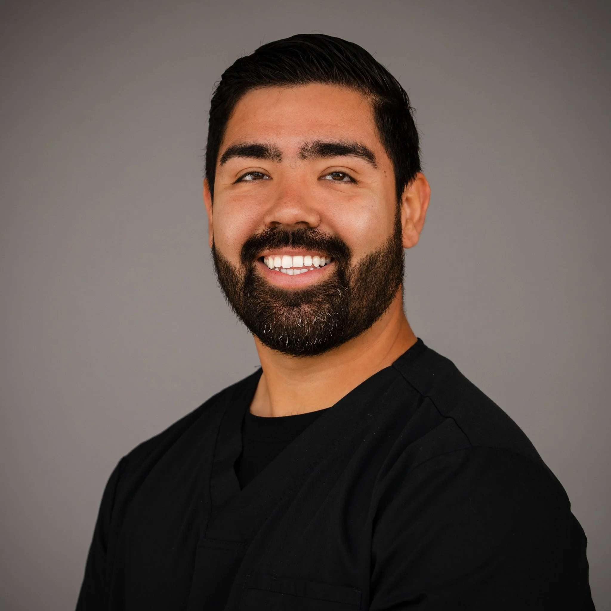 Smiling person with a beard against a brick wall background.
