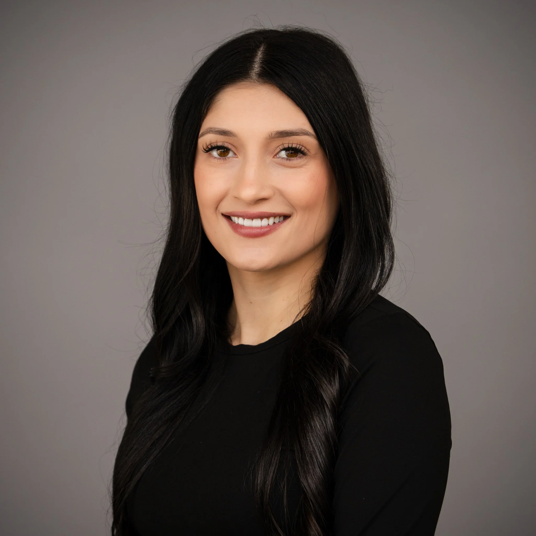 Smiling woman with long dark hair, wearing a black top, looking at the camera.