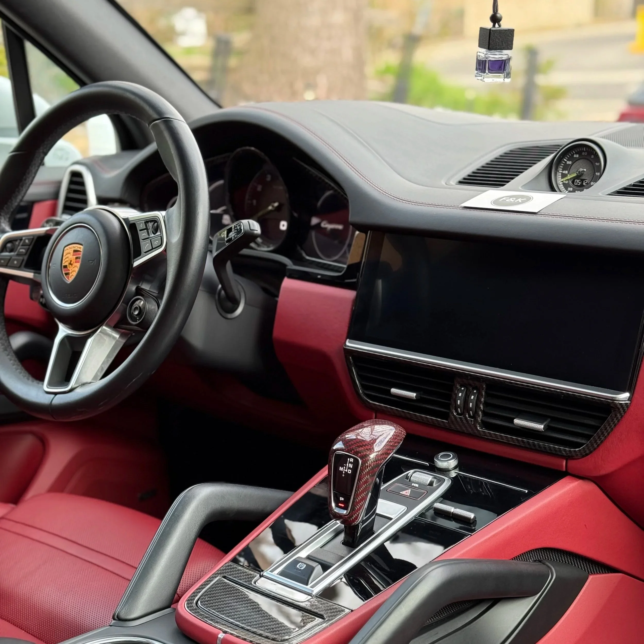 The interior of a luxury car showing the steering wheel with Porsche badge, the dashboard, center console, and gear shift, with a red interior and modern controls.