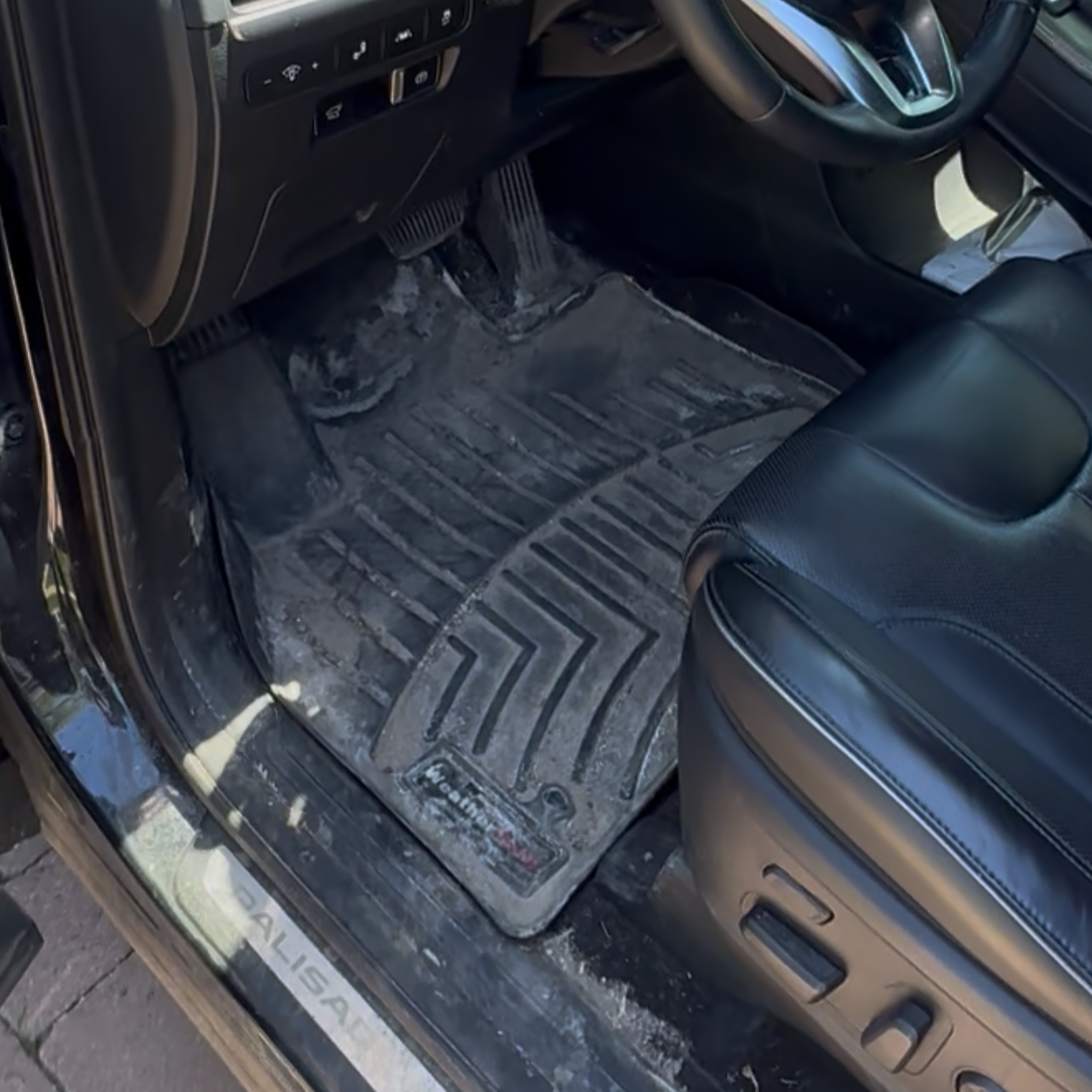Inside a vehicle showing the driver's side foot area, including the accelerator, brake pedal, and a dirty rubber floor mat.