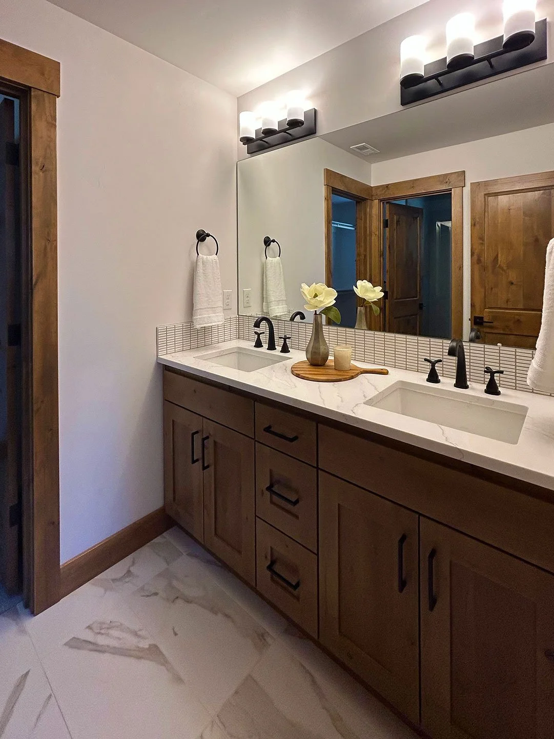 Bathroom with wooden vanity, double sink, large mirror, black fixtures, and modern lighting in Bend, Oregon.