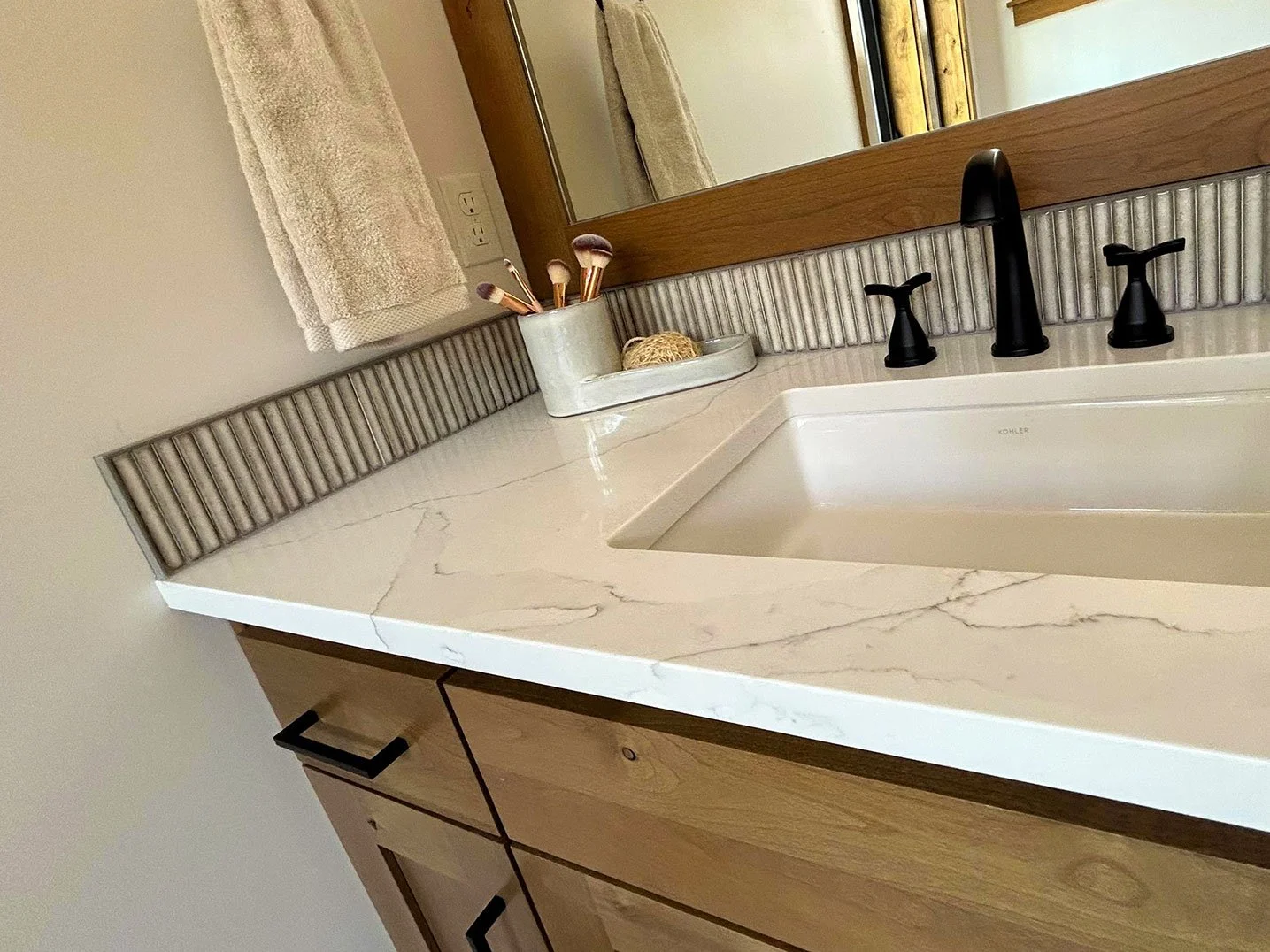 Bathroom countertop with a white marble surface, black faucet fixtures, a rectangular sink, a towel, and a toothbrush holder with brushes, against a large mirror in Bend, Oregon.