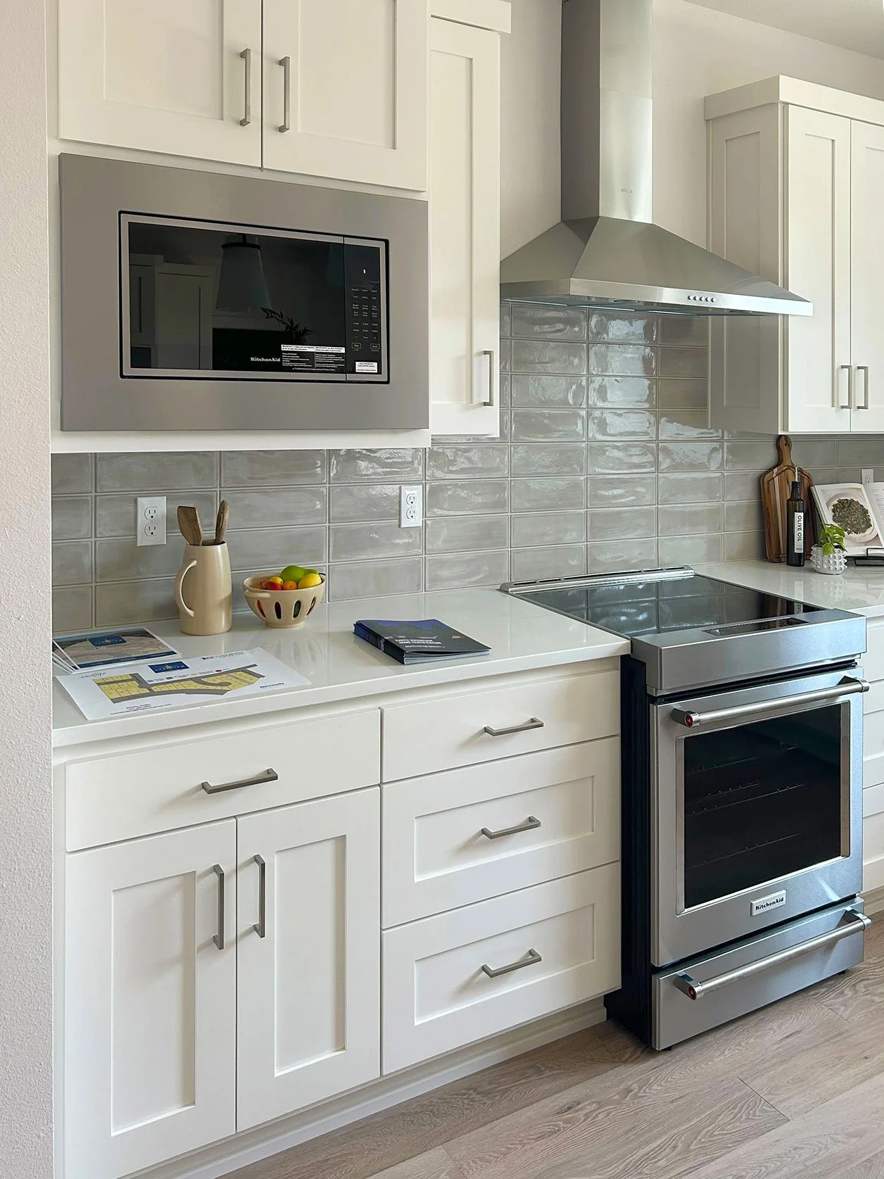 Modern kitchen with white cabinets, a stainless steel microwave, stove, and oven, beige tiled backsplash, and countertop with a bowl of fruit and a notebook in Bend, Oregon.