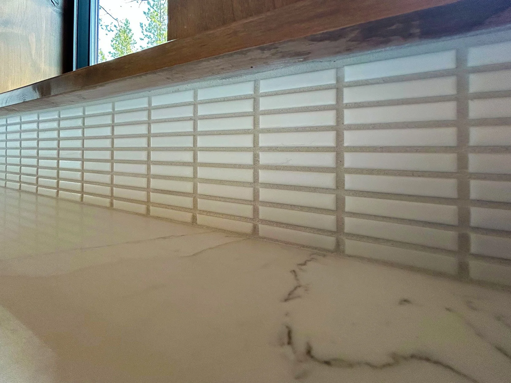 Close-up of a tiled wall near a window with a wooden ledge, showing white rectangular tiles with grout lines, and a marble countertop surface in the foreground in Bend, Oregon.
