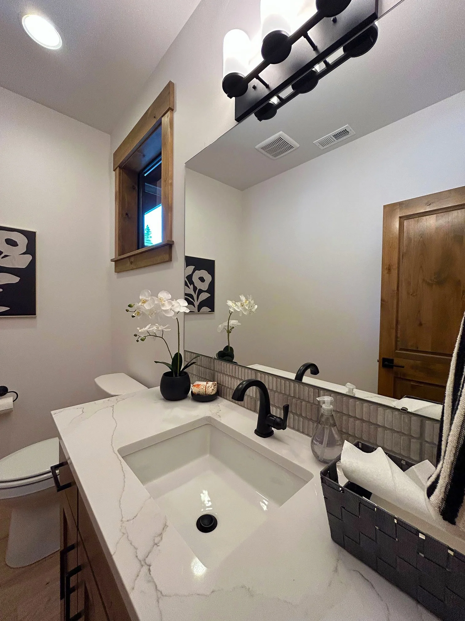 Bathroom with a white marble vanity, black fixtures, a mirror, and wall decor. A small window with wood trim is above the toilet in Bend, Oregon.