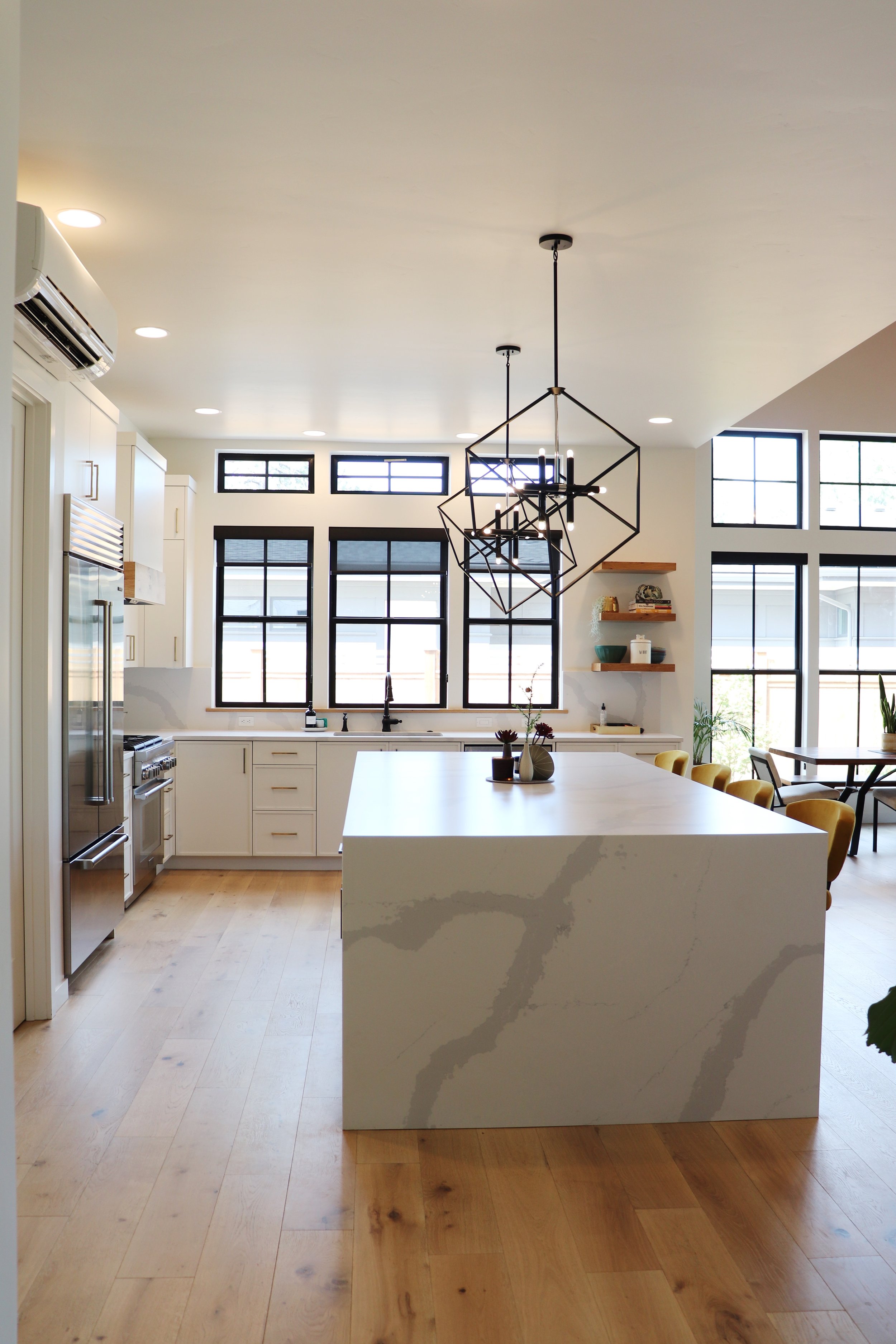 Modern kitchen with white cabinetry, black-framed windows, a large white marble island, wooden flooring, and geometric pendant lighting in Bend, Oregon.