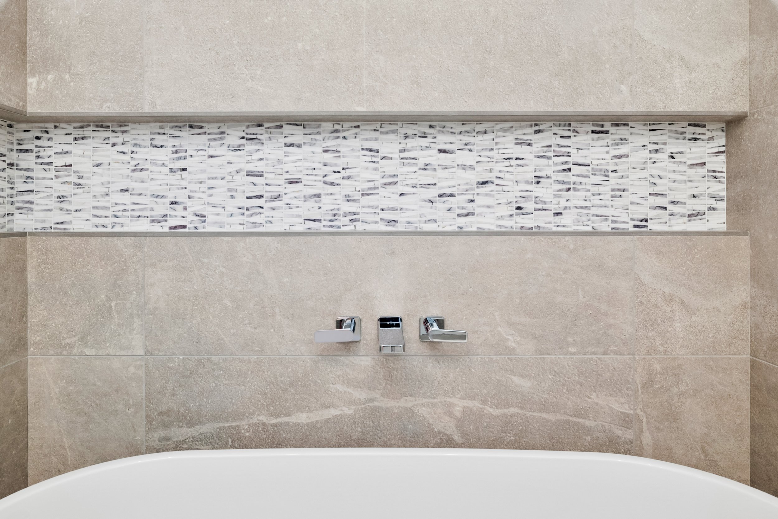 Close-up of a bathroom bathtub faucet and decorative tile border on a beige tiled wall in Bend, Oregon.