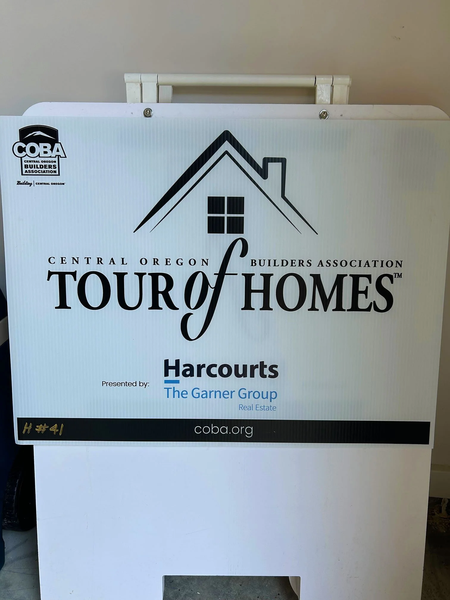 Sign for House Tour event organized by Central Oregon Builders Association, presented by Harcourts, with the web address coba.org.