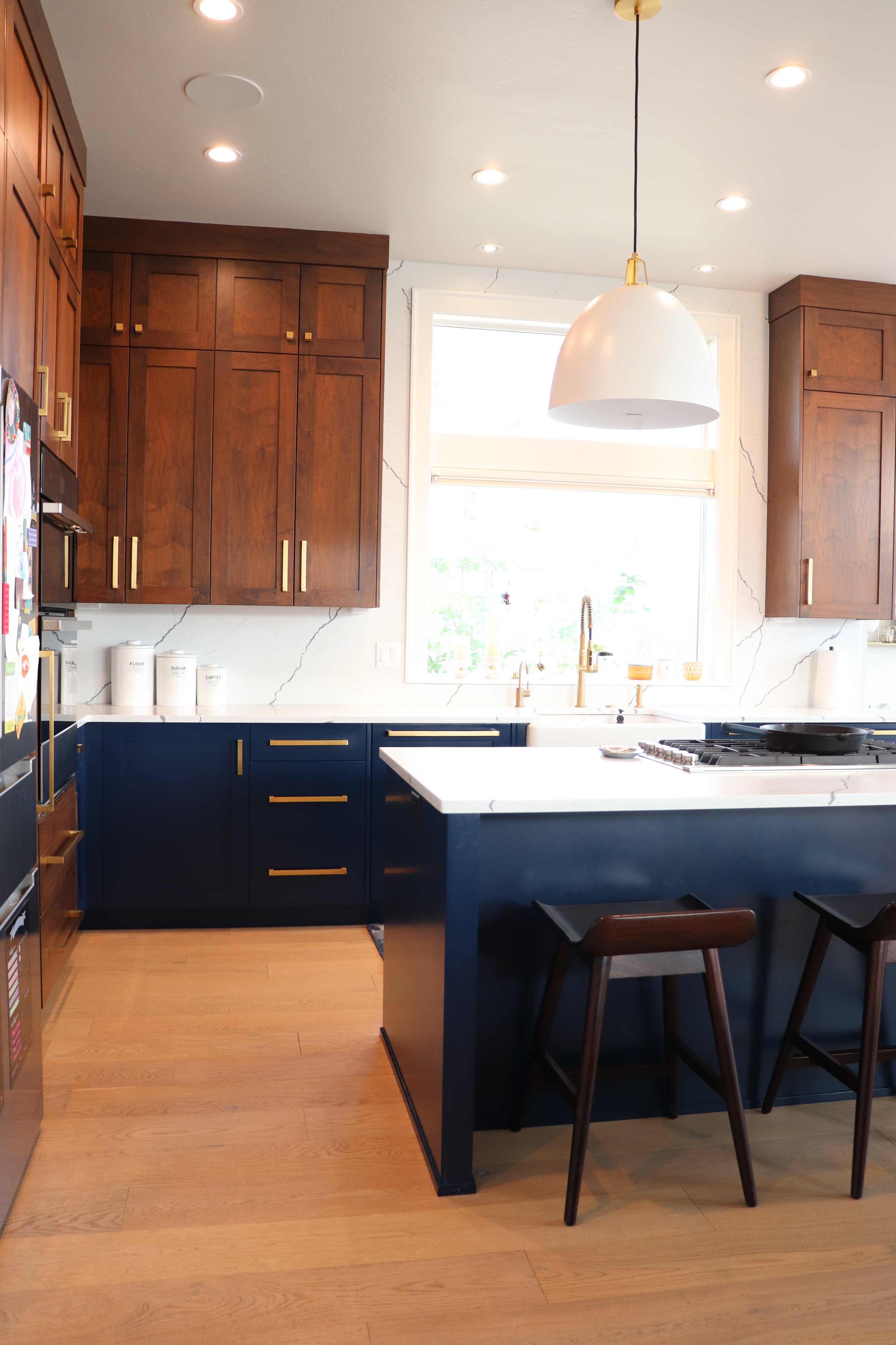 Modern kitchen in Bend, Oregon with wood cabinets, navy blue lower cabinets, white marble countertops, and a large window above the sink.