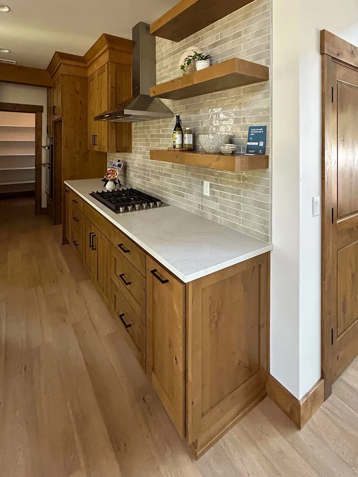Wooden kitchen cabinets with a white countertop, stove, brick backsplash, and open wooden shelves with decorative items in Bend, Oregon.