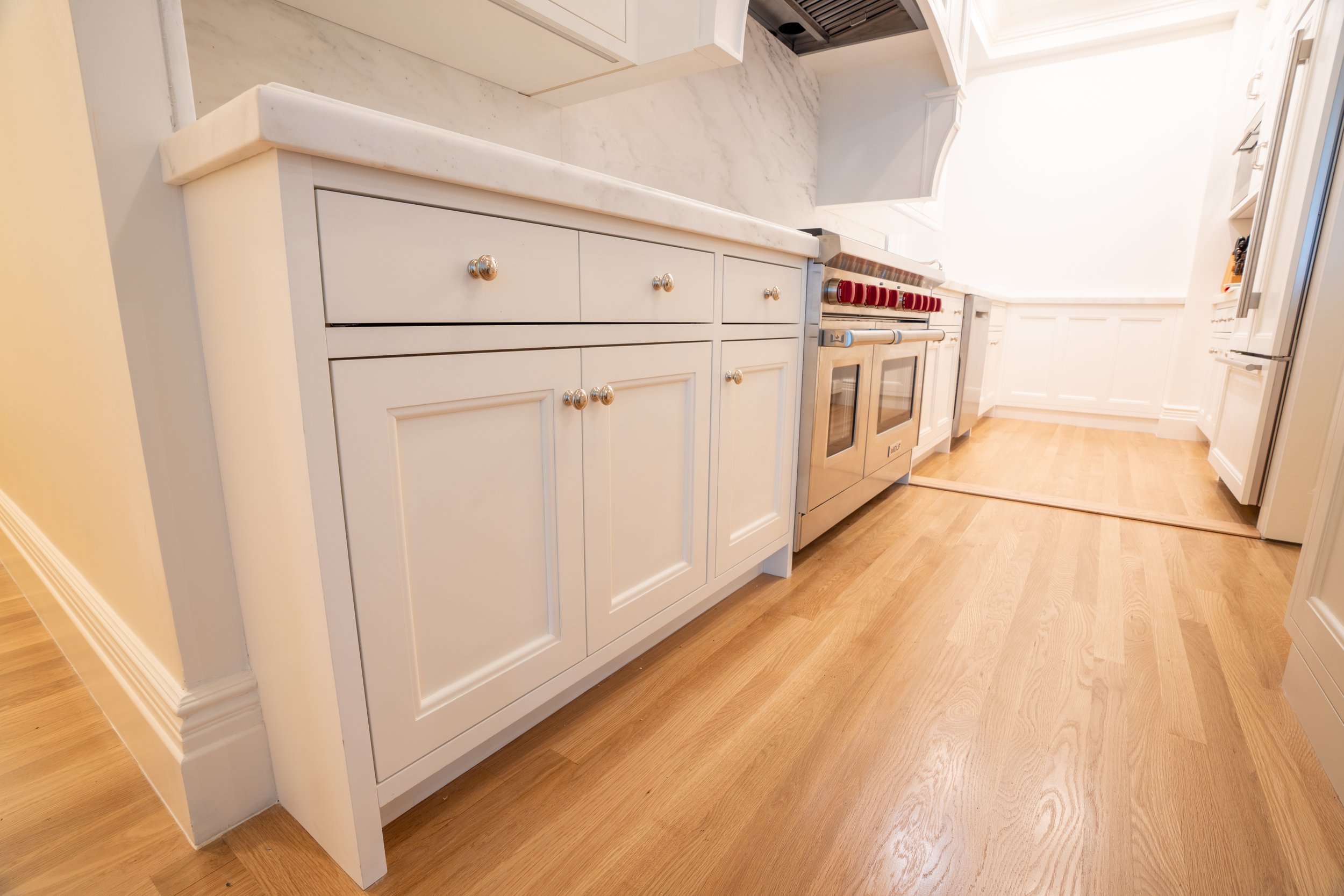 Modern kitchen with white cabinets, hardwood flooring, stainless steel oven, and marble countertops.