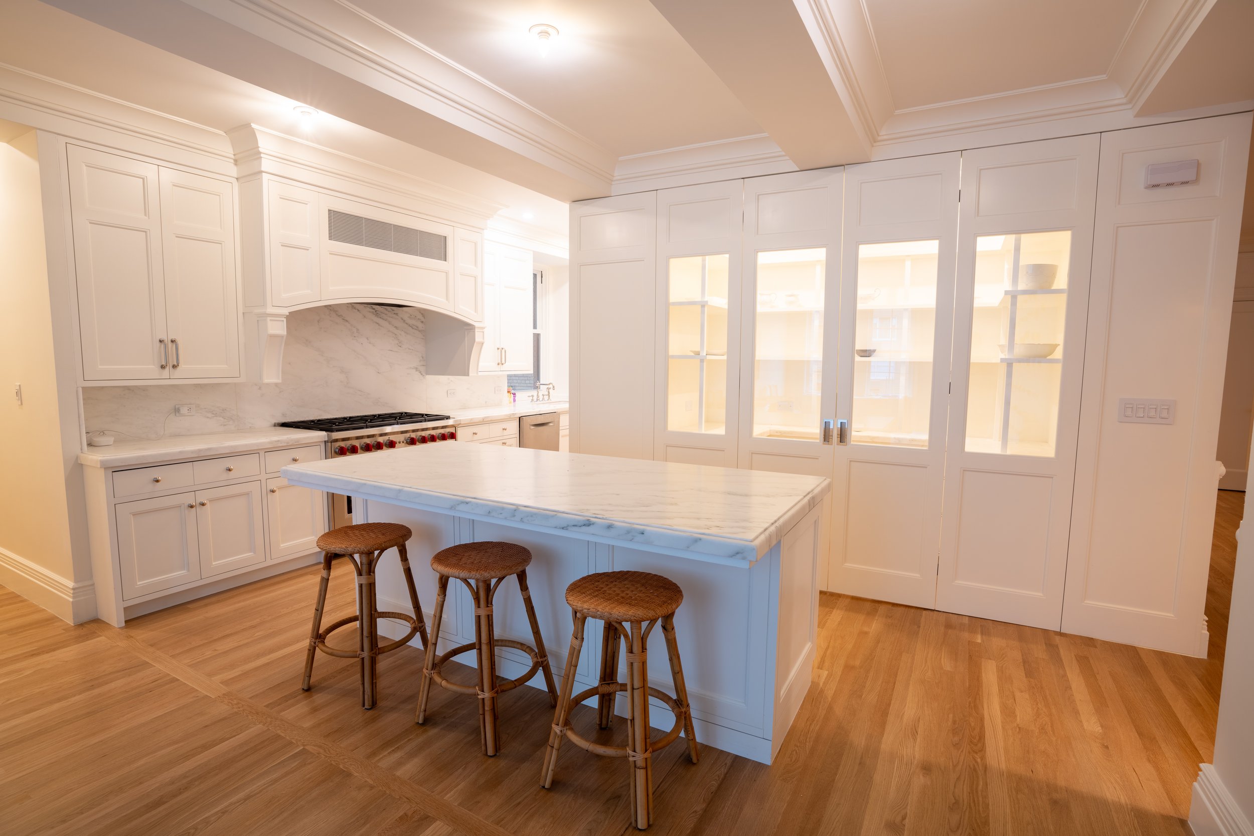 Modern kitchen with white cabinets, marble countertops, island with wicker stools, and stainless steel appliances.