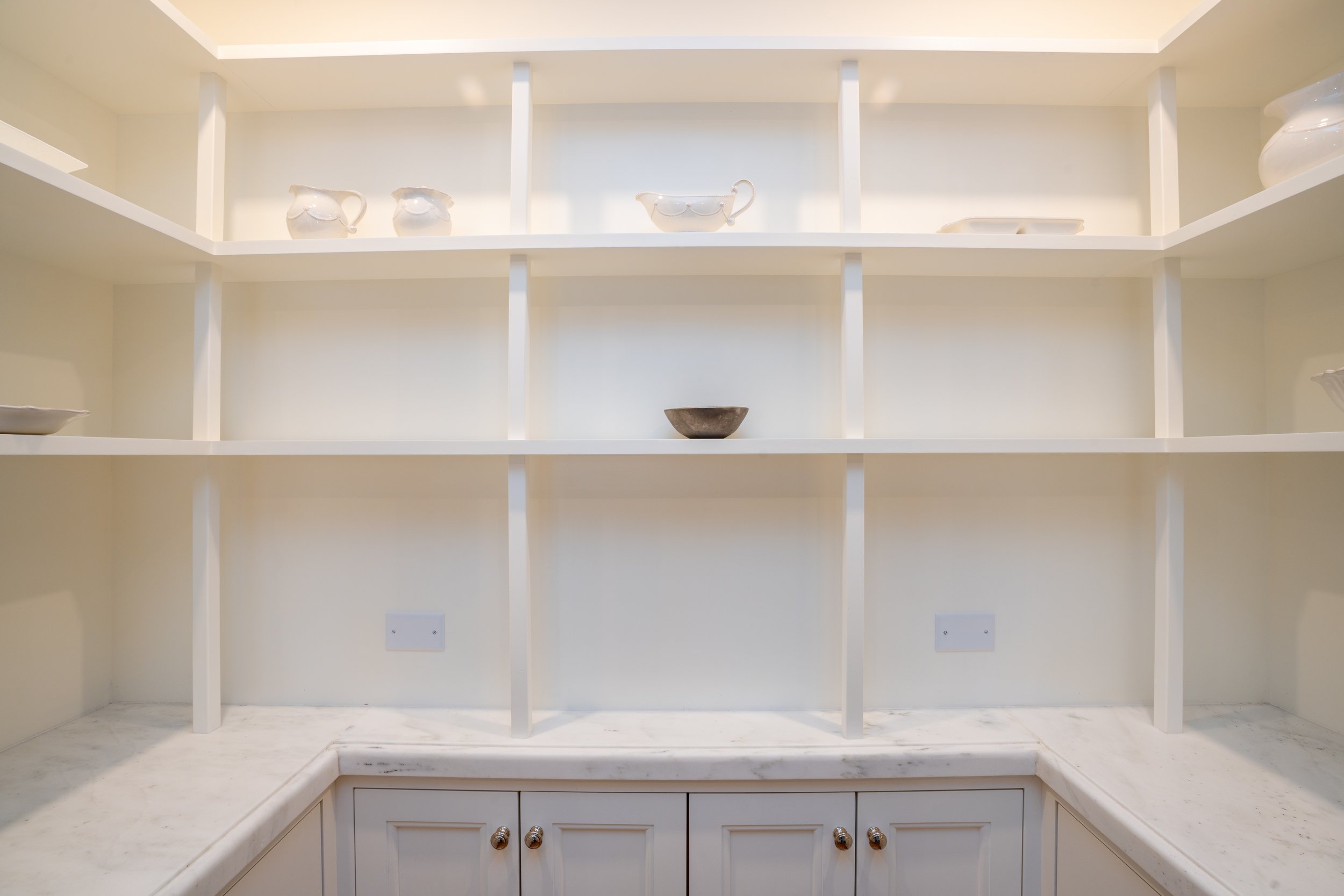 Minimalist white kitchen shelves with various white ceramic dishes and a gray bowl on marble countertops.