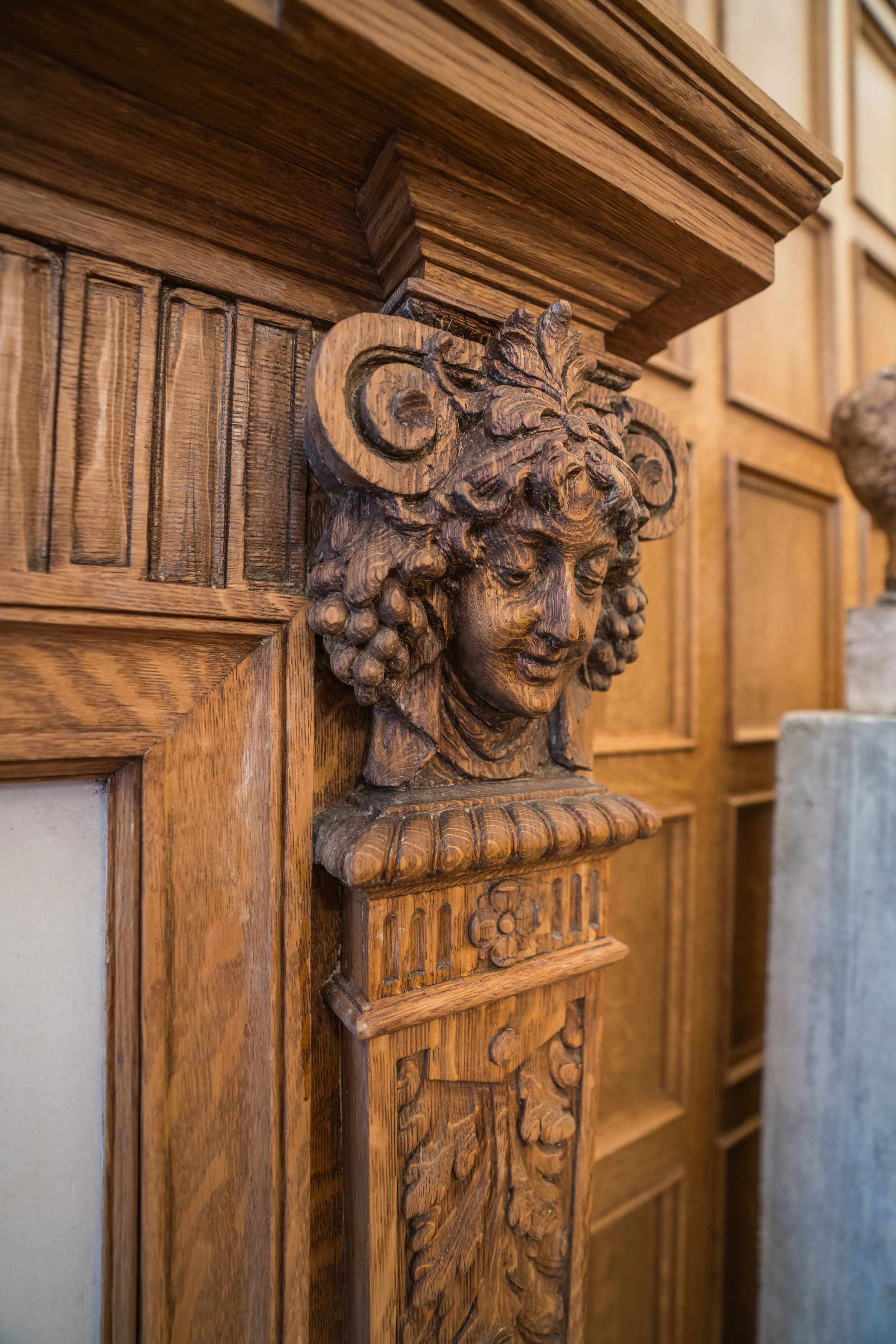 Decorative wood carving of a woman's face with curly hair and ornate floral details on a wooden panel.