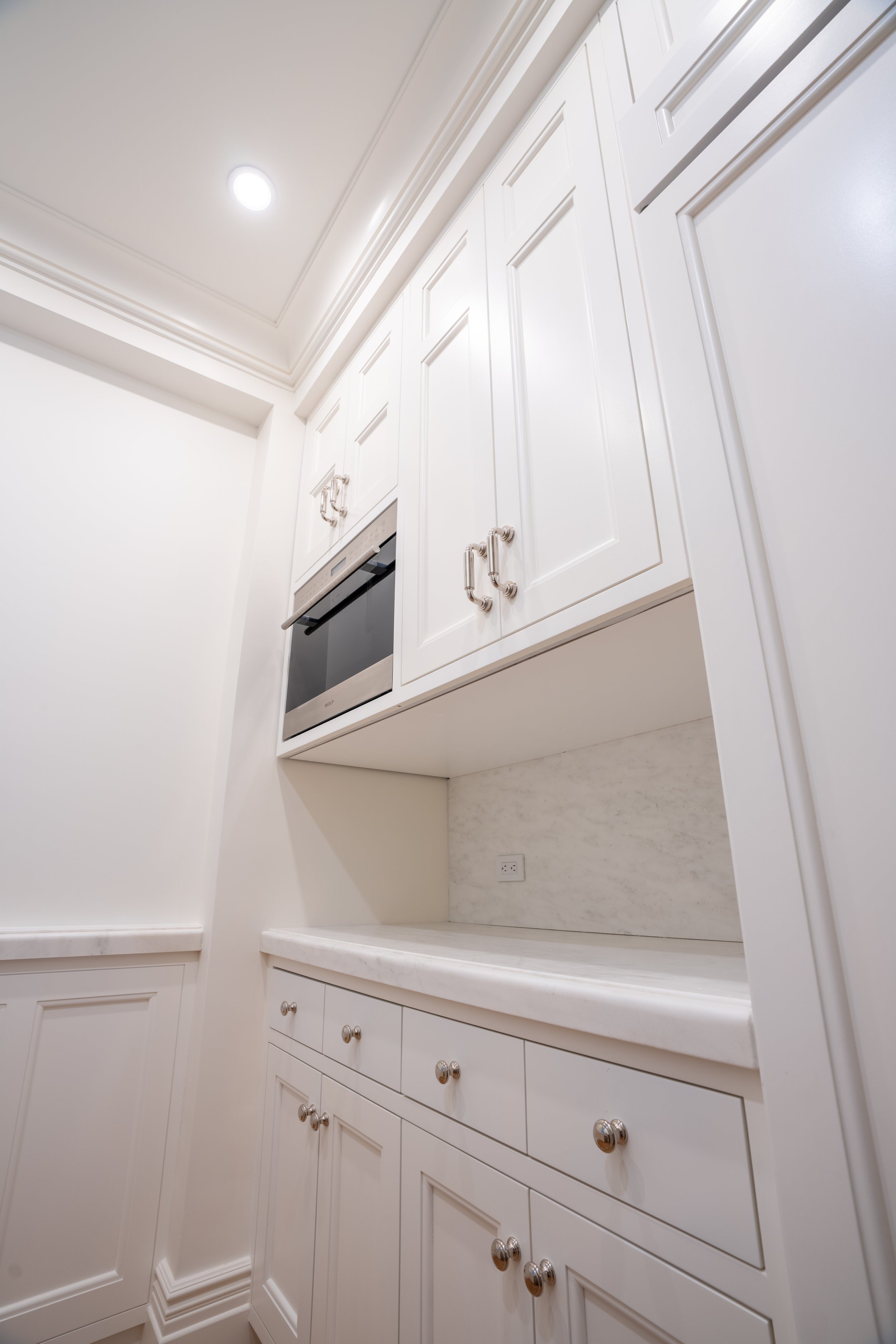 Modern kitchen with white cabinetry, a built-in oven, marble countertop, and recessed lighting.