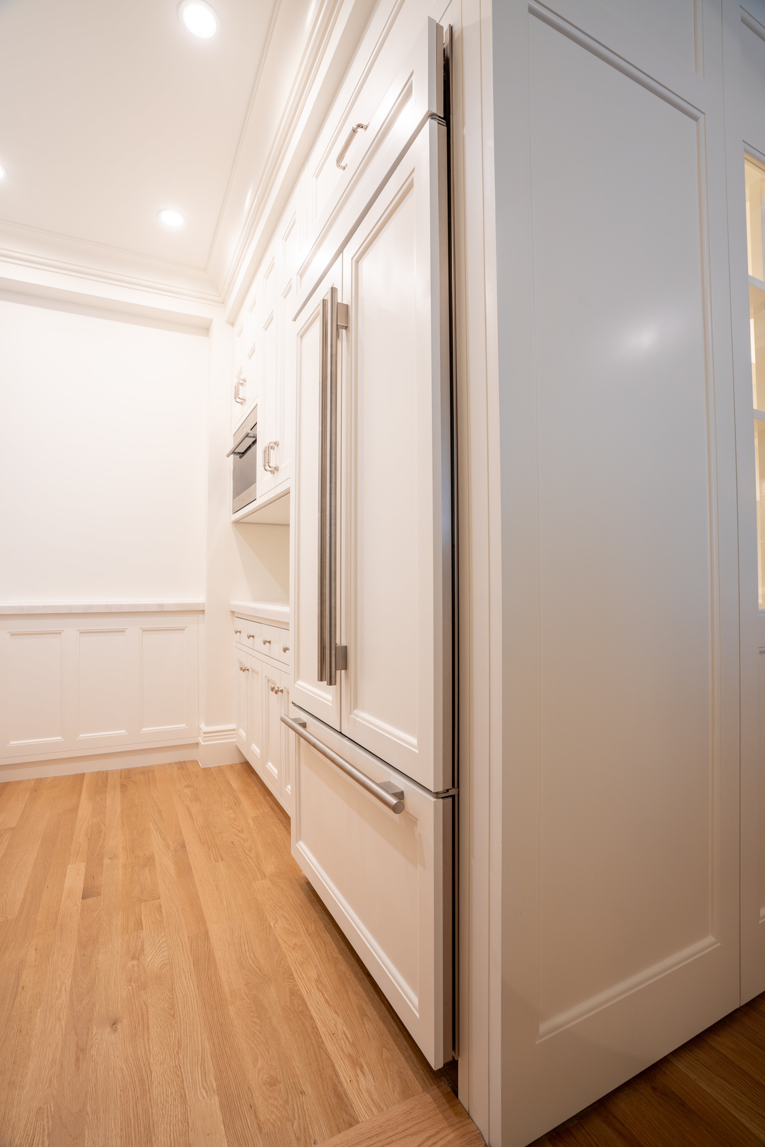 Modern kitchen interior with white cabinets, stainless steel refrigerator, and wood flooring.