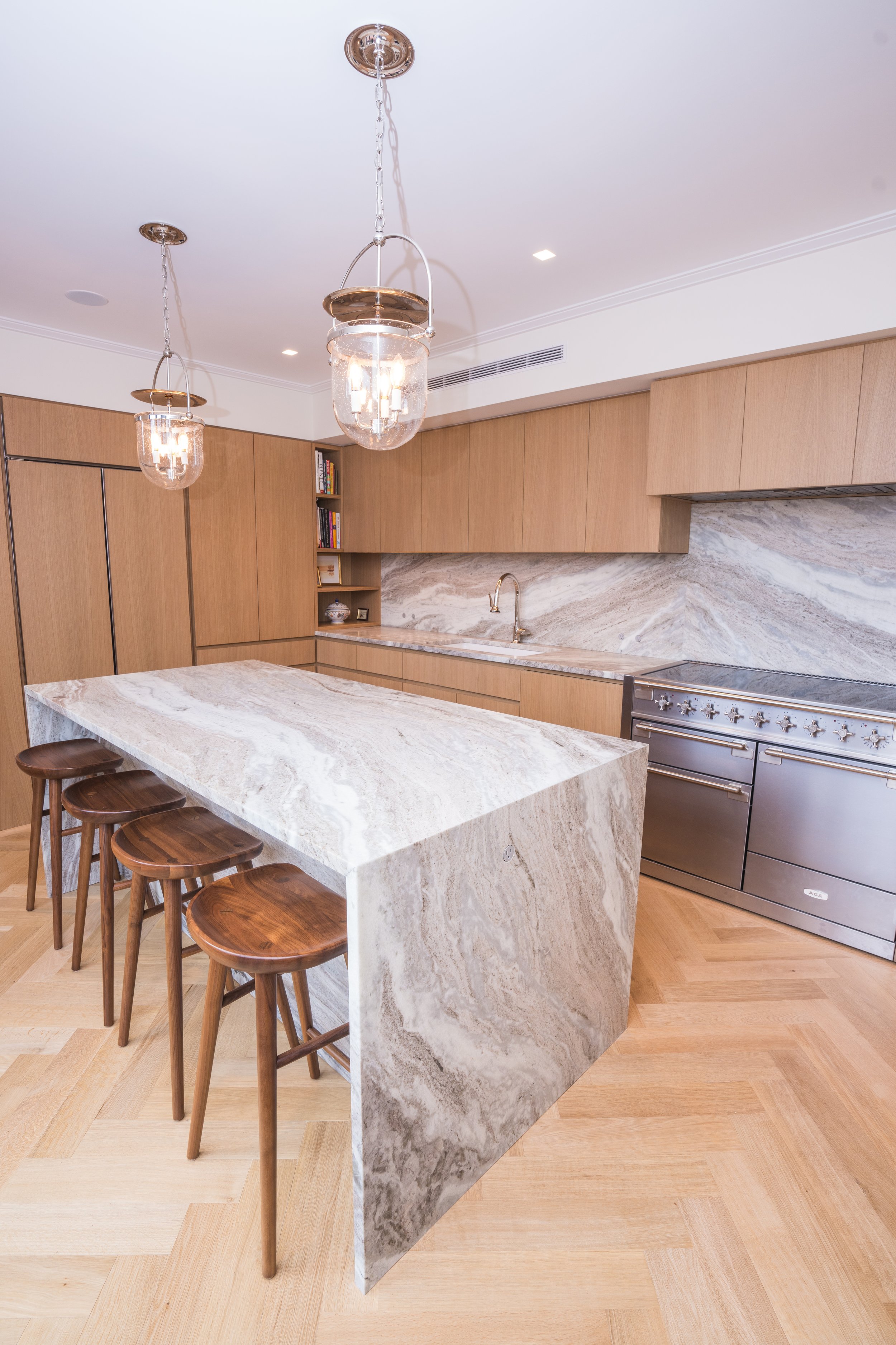 Modern kitchen with marble island, wooden cabinets, stainless steel appliances, and pendant lighting.