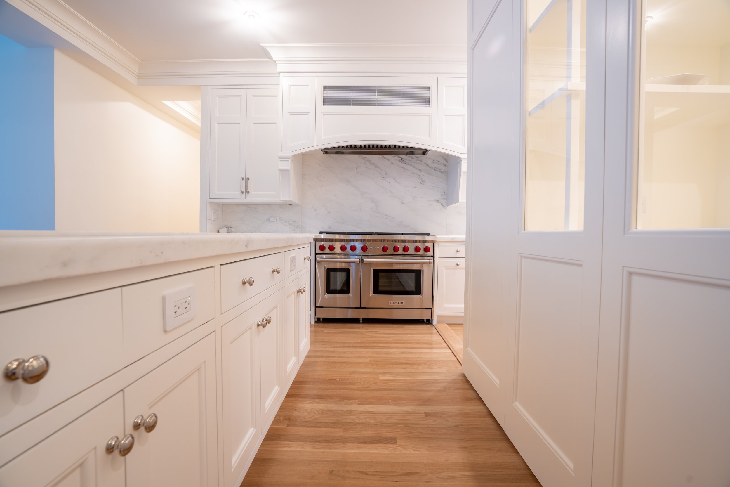 Modern kitchen with white cabinets, marble countertops, stainless steel oven, and hardwood floors.