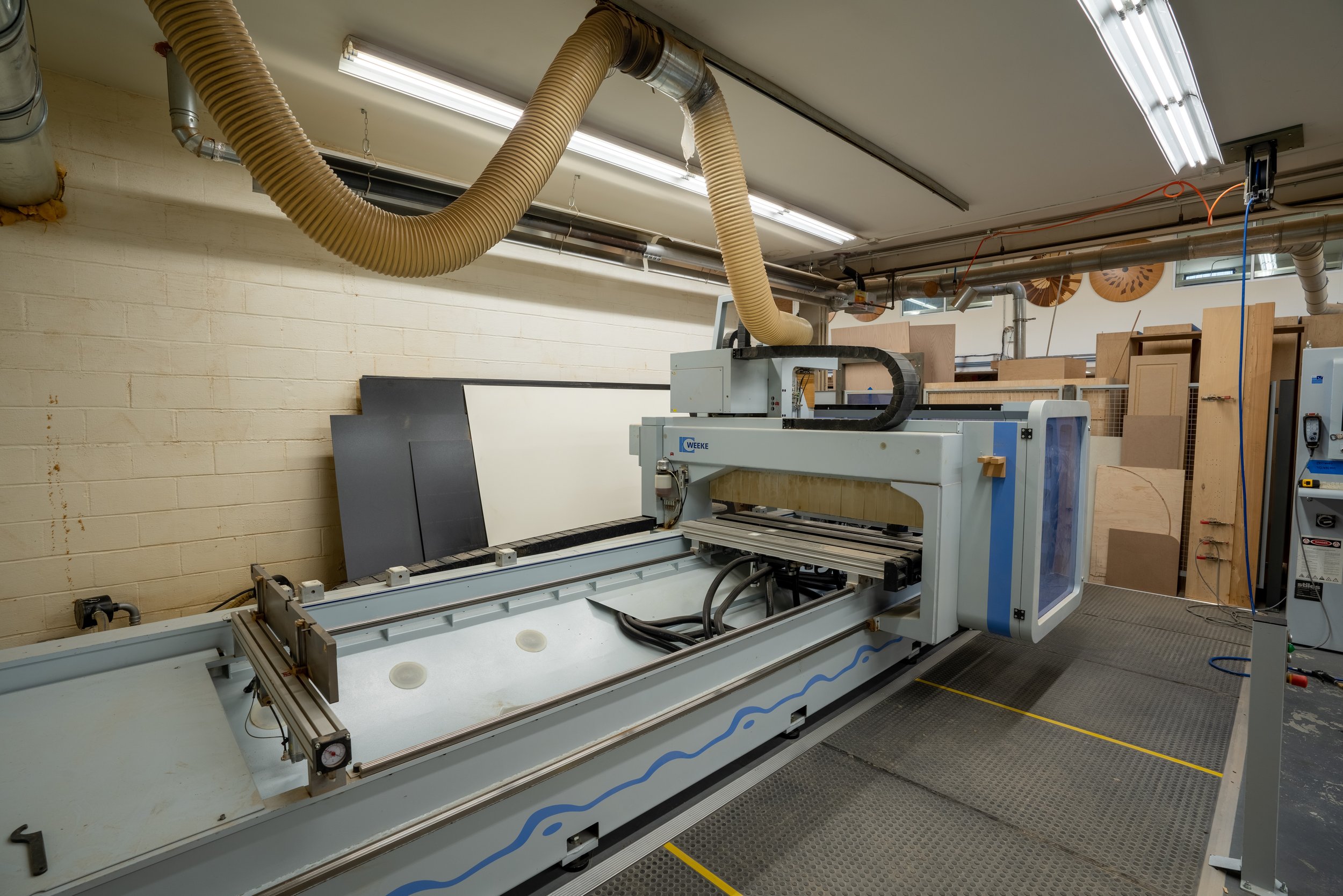 CNC router machine in a workshop with wooden boards and duct system.