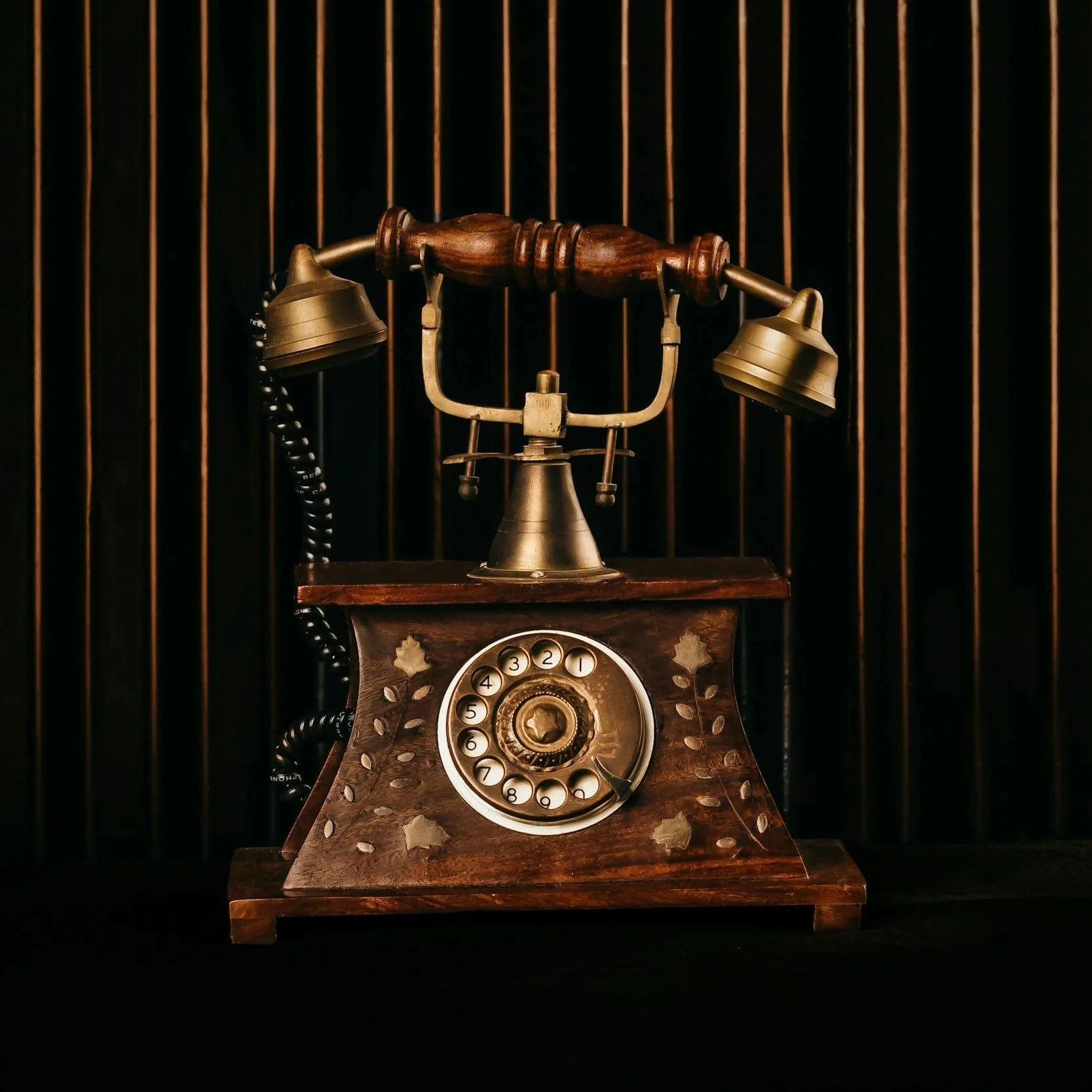 Vintage rotary phone with a brass and wood design, set against a dark background with wooden bars.