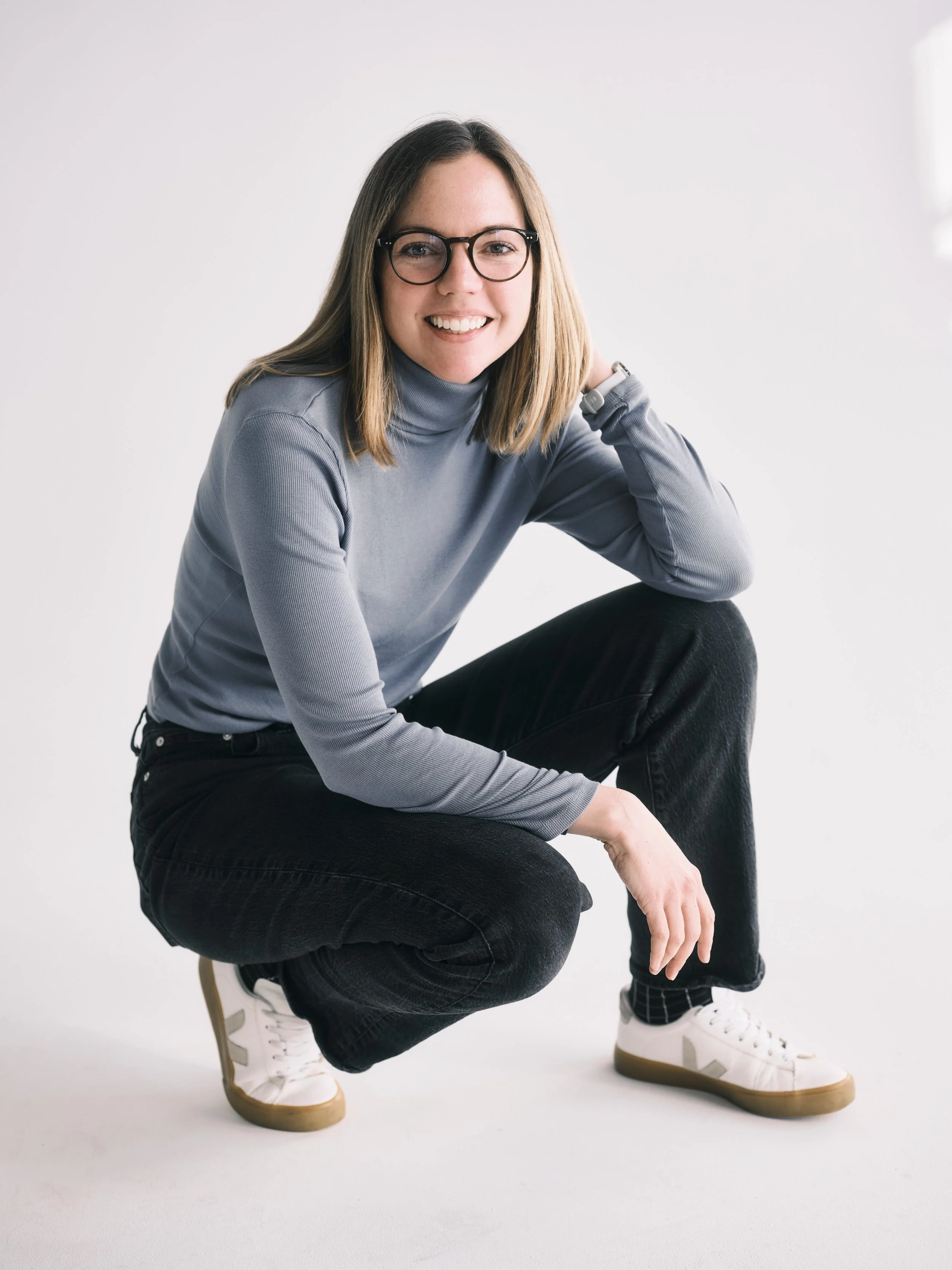 Laurel Bybee sitting casually in gray turtleneck and dark jeans, wearing glasses