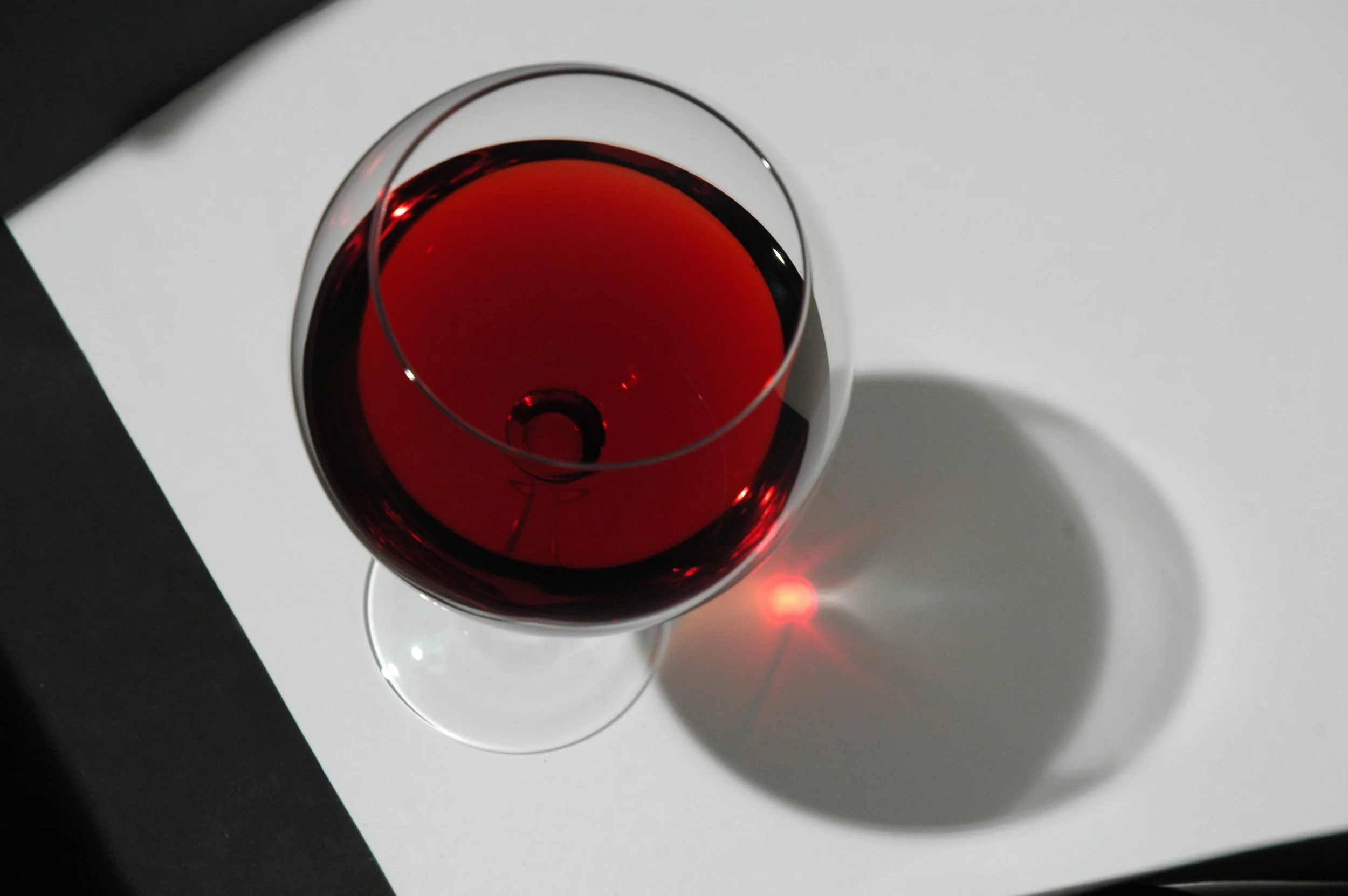 Calice di vino rosso su una superficie bianca con ombra proiettata.