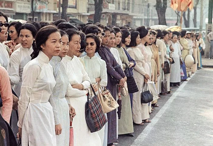 Group of women lined up on the sidewalk, dressed in traditional clothing, waiting or observing something.