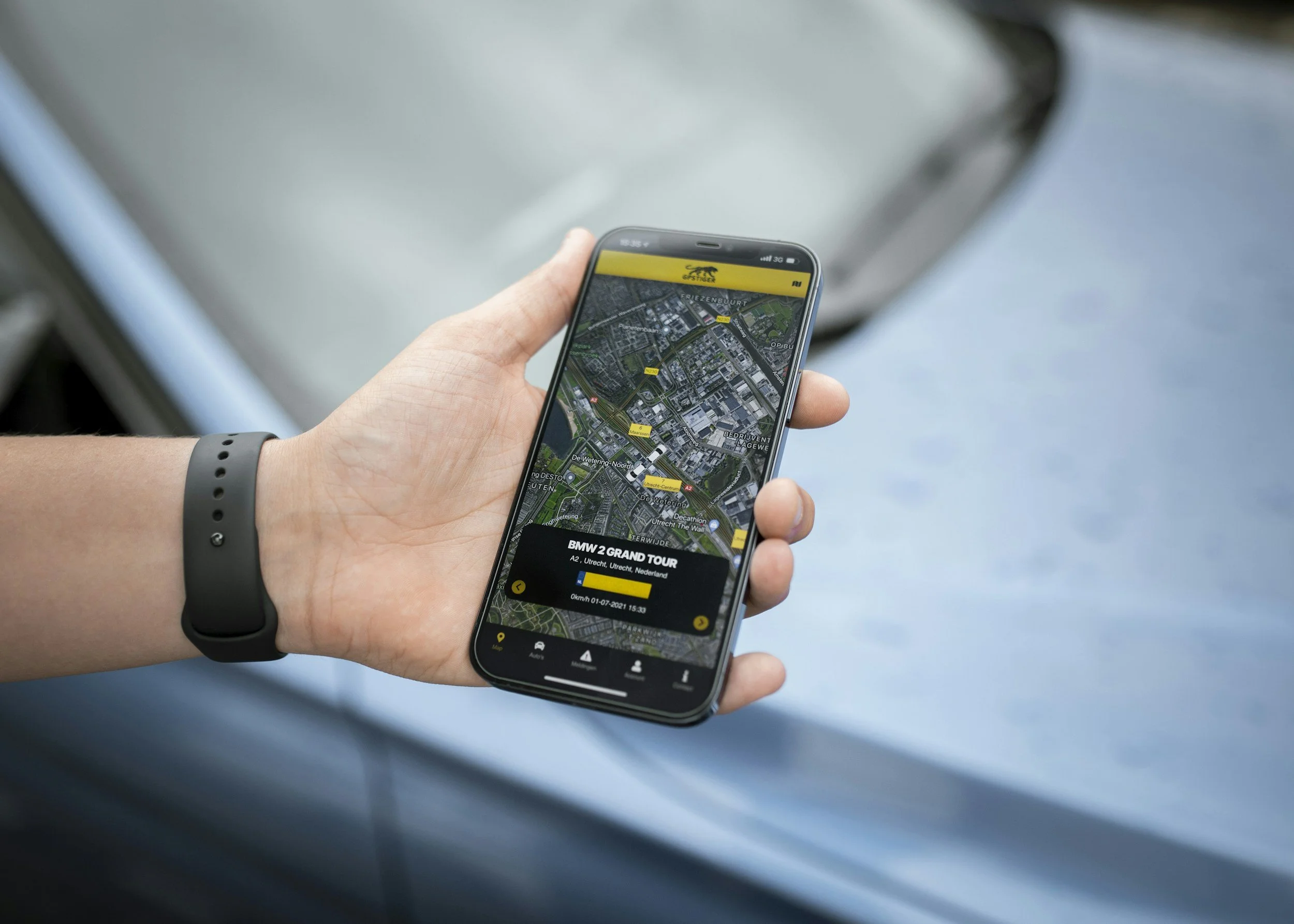 Hand holding a phone with a TAG tracking app open in front of a car