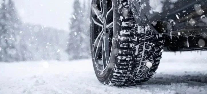 The front tire of a black vehicle driving though snow and ice