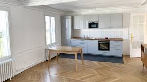Cuisine moderne avec parquet en bois, meubles blancs, table en bois, et four intégré.