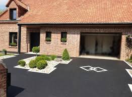 Entrée d'une maison en briques rouges avec un garage ouvert, jardin aménagé, et allée pavée.