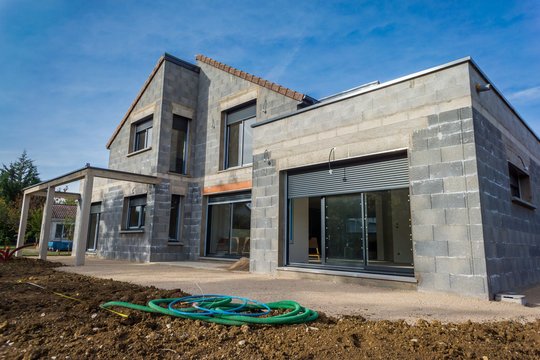 Maison en construction avec murs en parpaings et fenêtres installées.