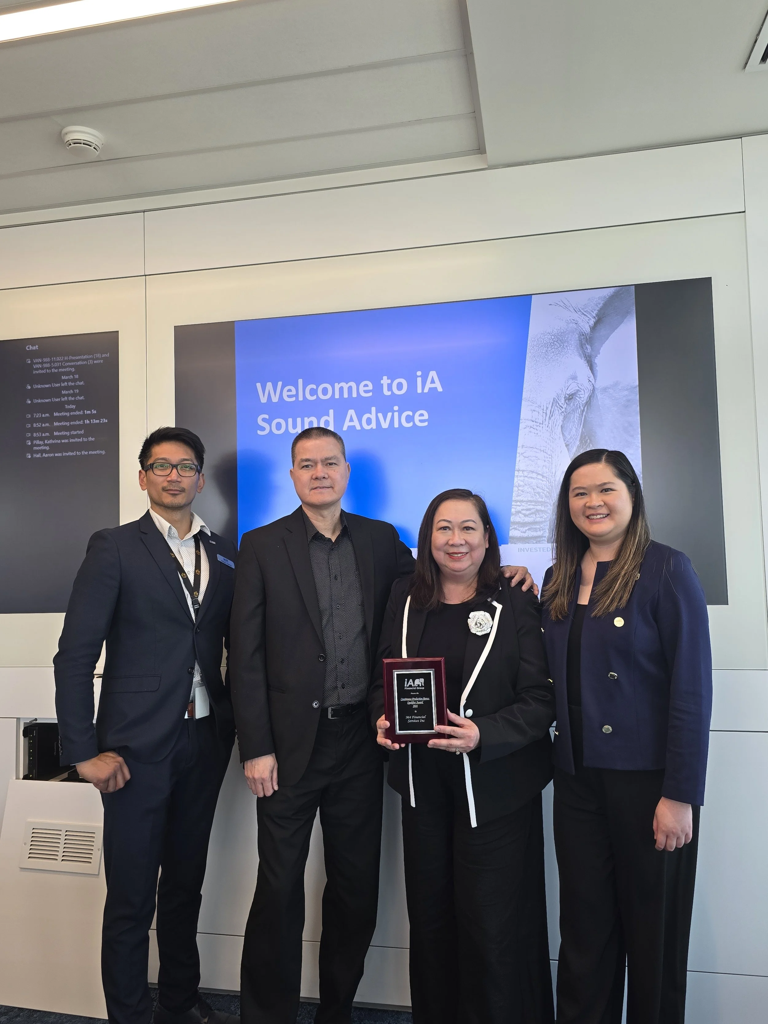 Four people standing together in front of a screen that reads 'Welcome to iA Sound Advice,' with a graphic of an elephant. One woman in the center holds an award plaque.