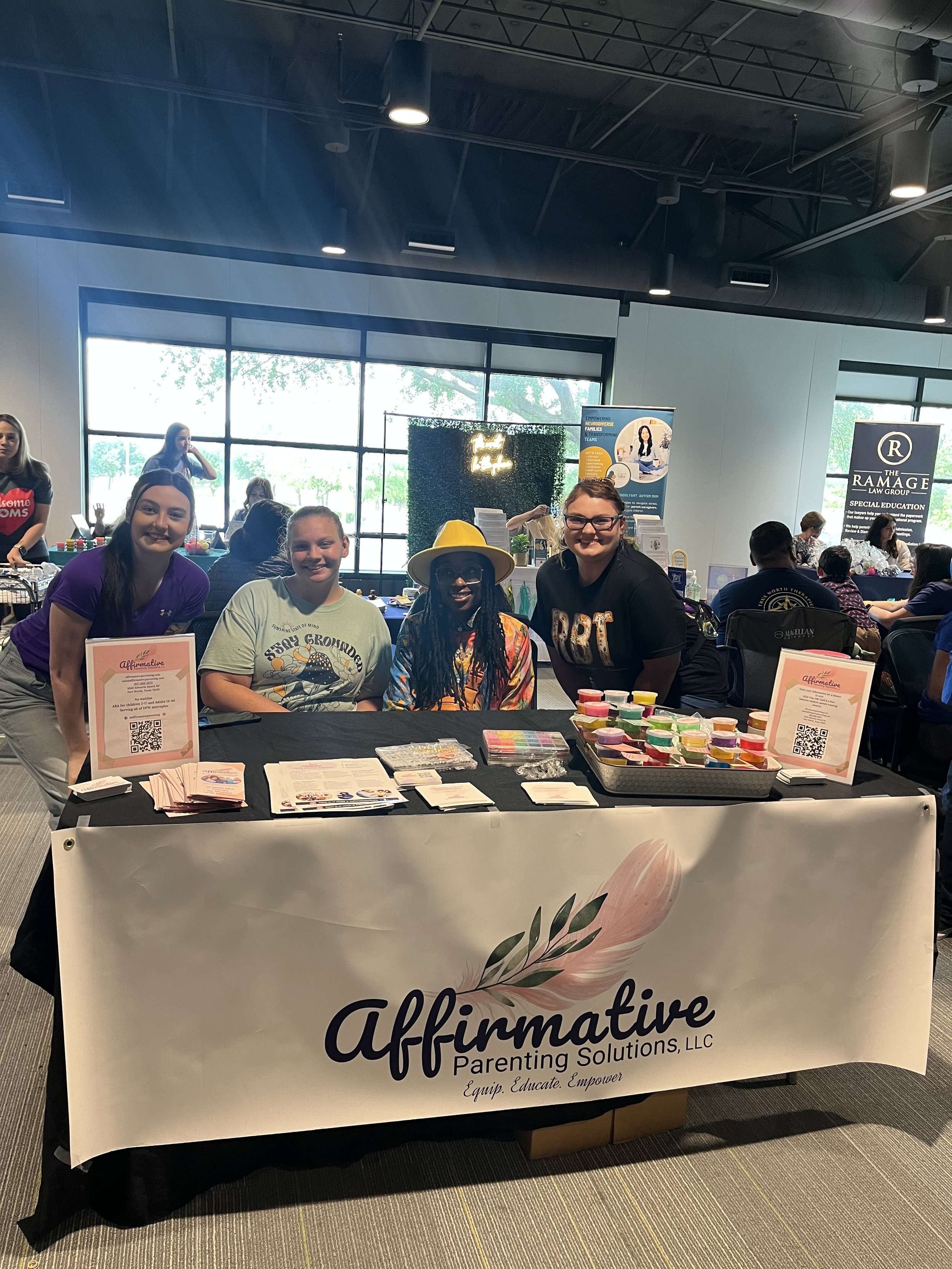 Group of four women at an informational booth for Affirmative Parenting Solutions, LLC, with sample materials and informational flyers on the table.