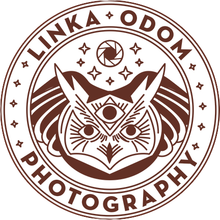 A circular logo for Linka Odom Photography featuring a stylized fox face with three eyes, surrounded by stars, a camera aperture symbol, and a landscape background.