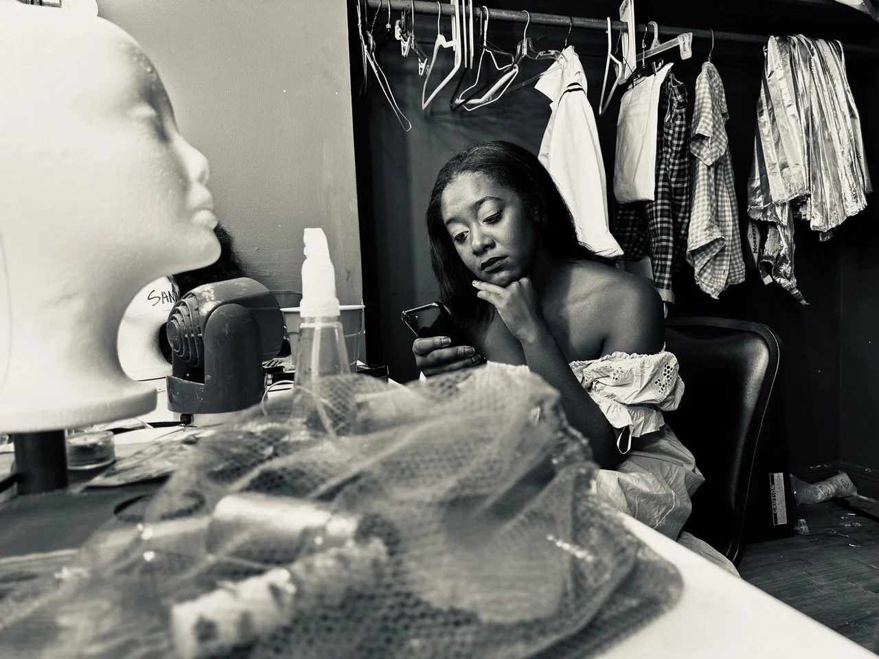 Close-up of a woman with medium brown skin, dark hair, and neutral expression, outdoors with blurred background.