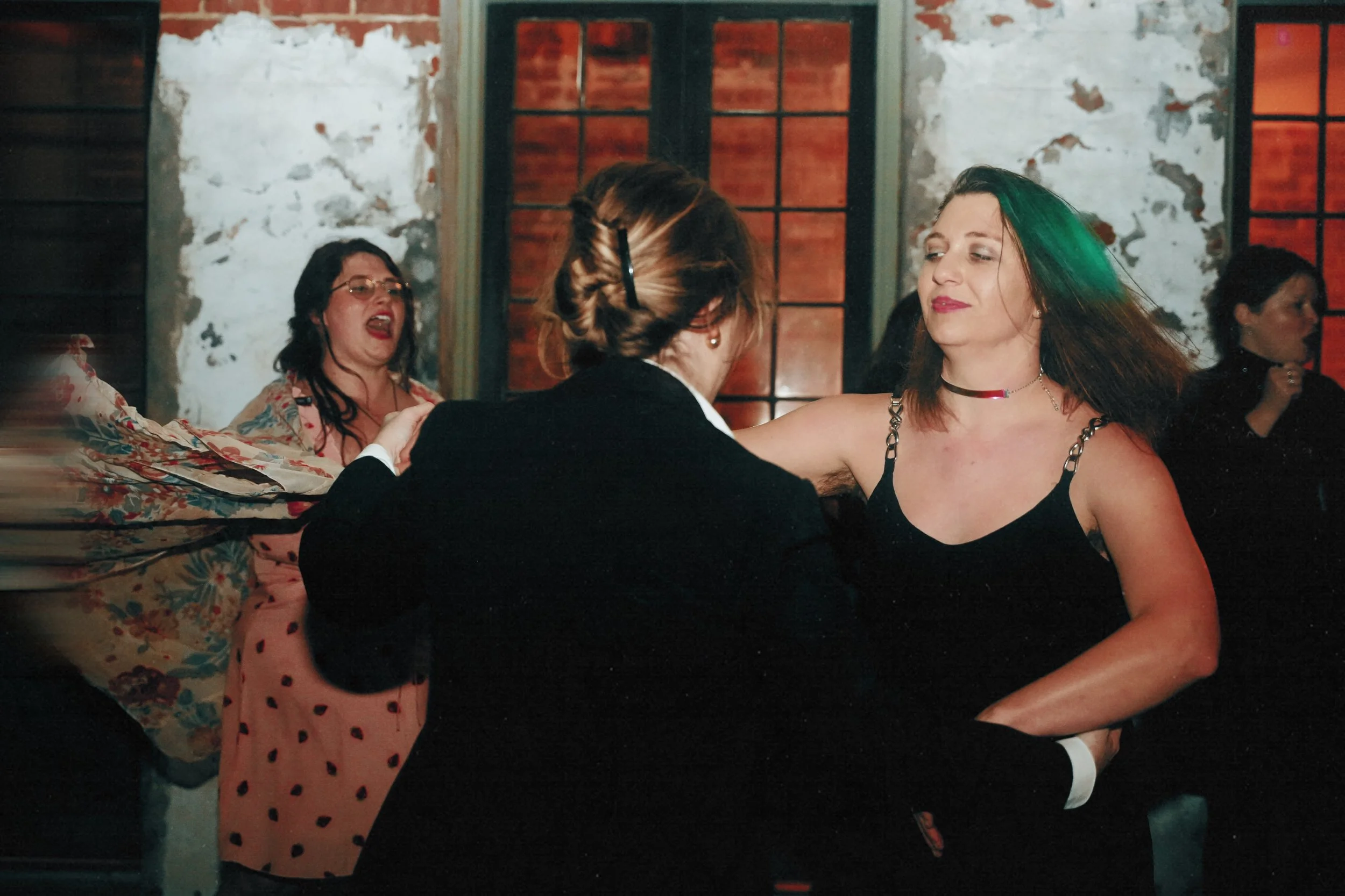 People dancing closely together at a party or dance event in a decorated indoor space with brick and wood walls.