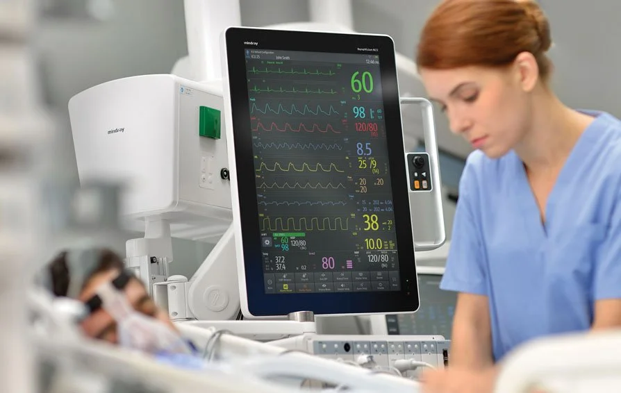 Healthcare professional monitoring a patient's vital signs on a large digital screen in a hospital setting.