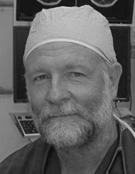 A man with a beard and mustache, wearing a surgical cap, in a medical setting.